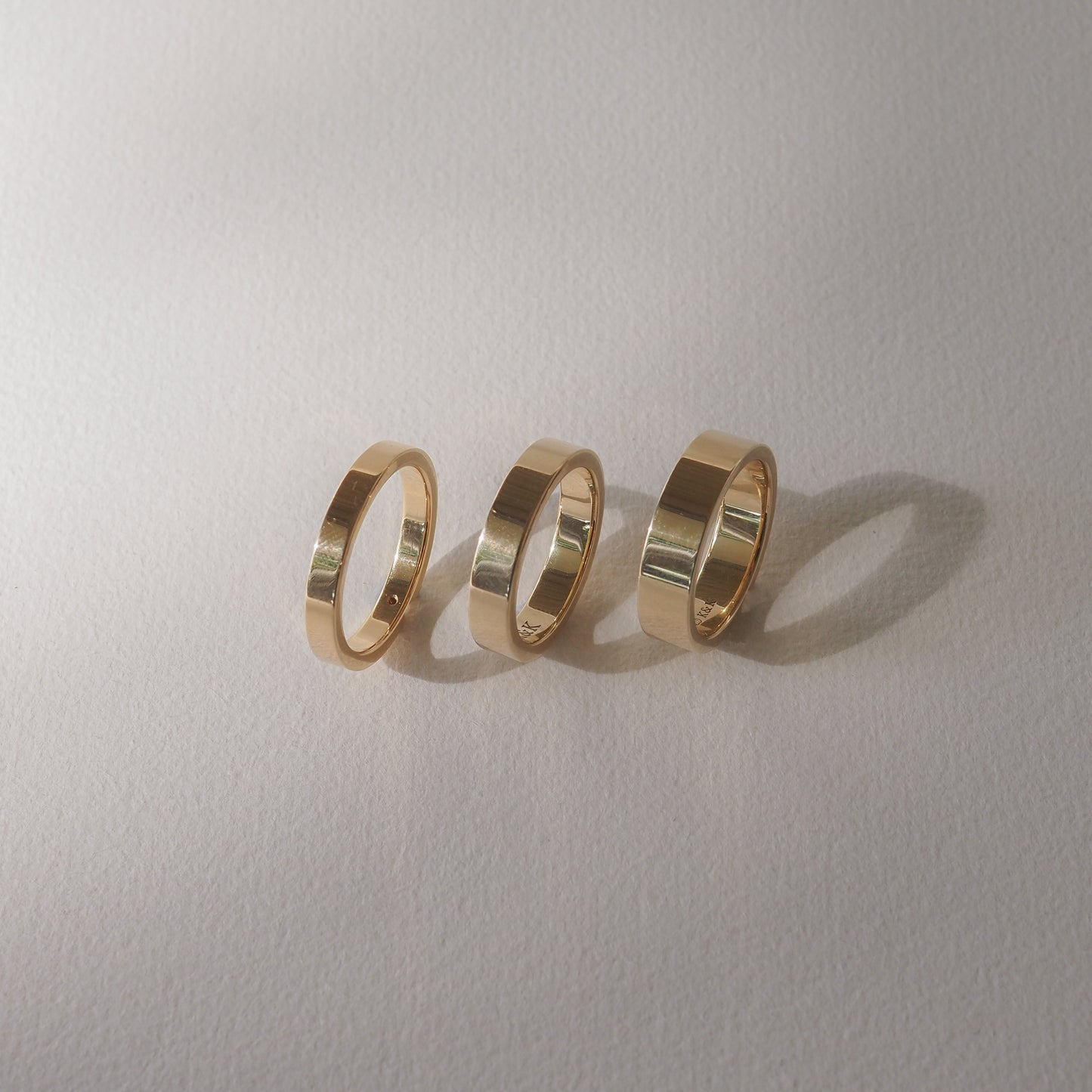 Three gold rings with polished finishes on a soft, light grey background, casting subtle shadows.