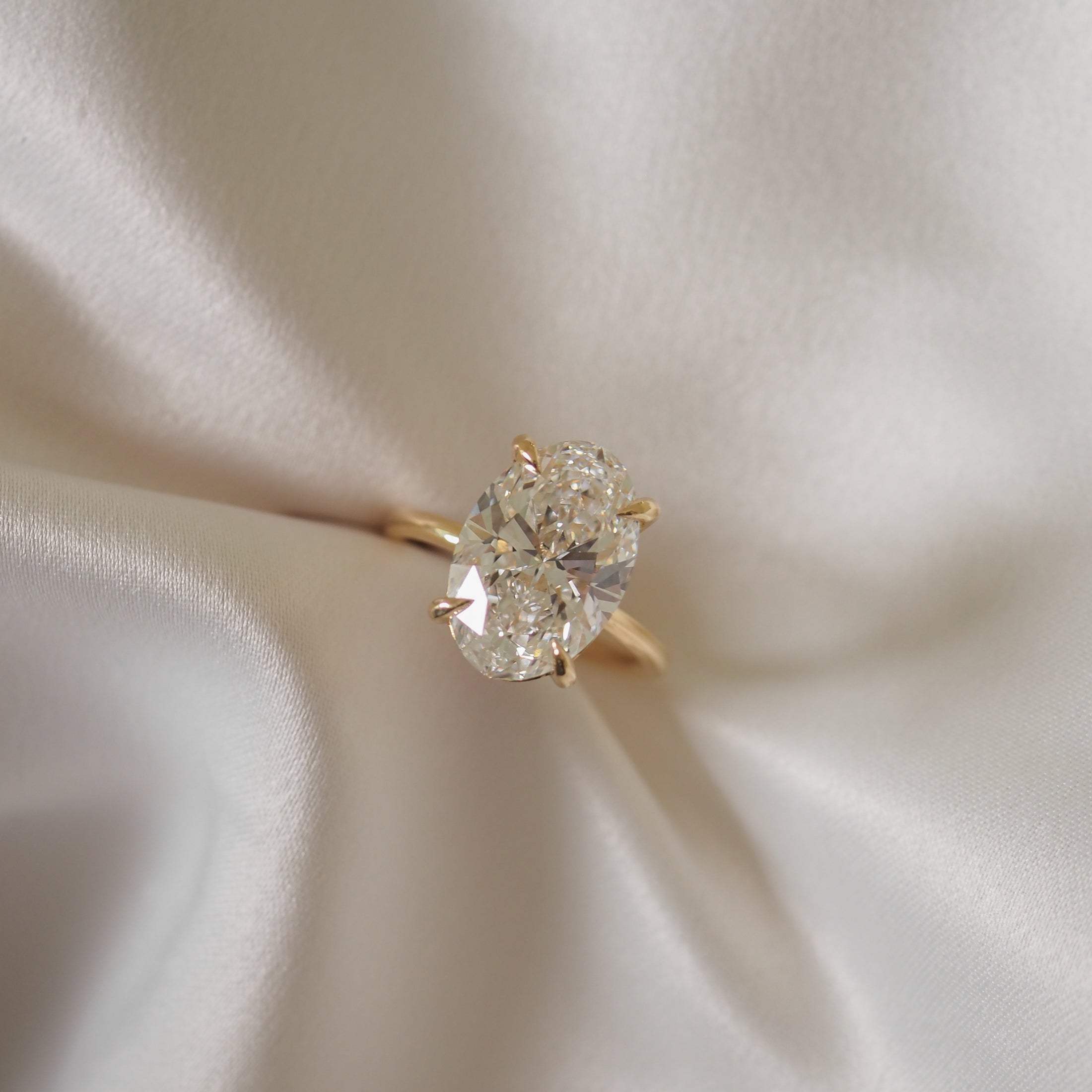 Oval diamond ring with gold band, elegantly displayed on silky fabric backdrop, highlighting luxury jewellery design.