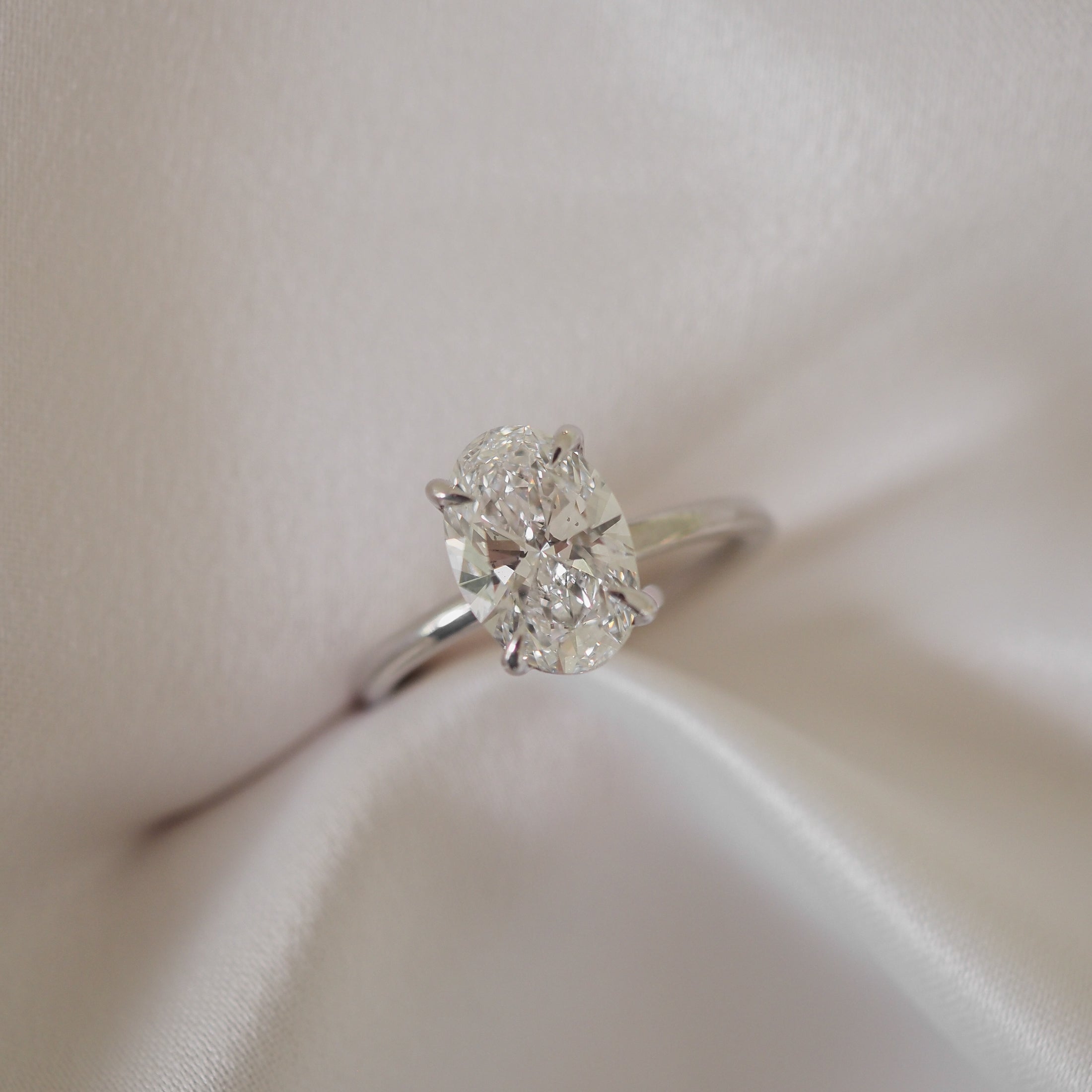 Oval diamond engagement ring on silky fabric backdrop, highlighting its brilliance and luxury appeal. Perfect for high-end jewellery lovers.
