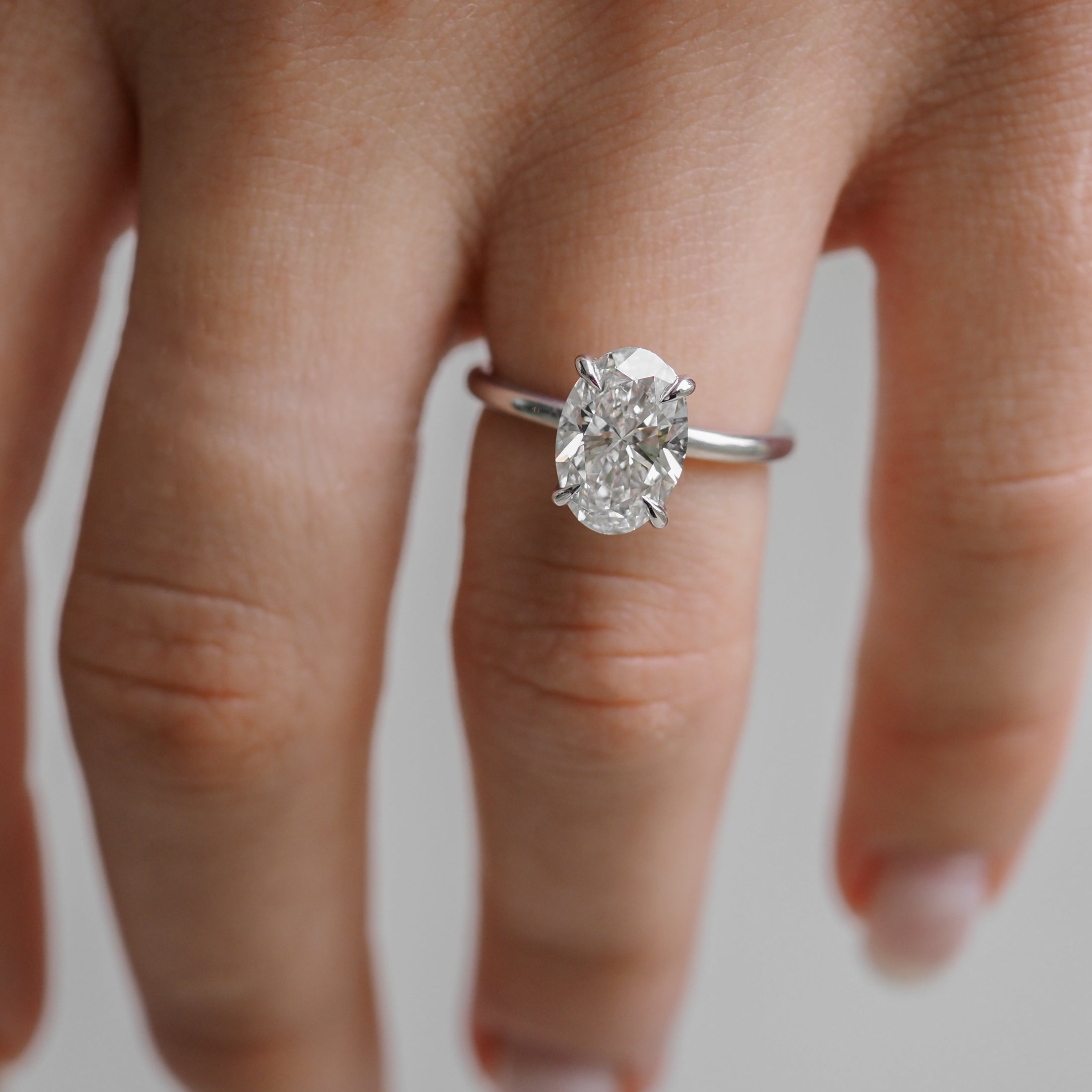 A hand wearing an elegant engagement ring with a large oval diamond set on a sleek silver band, showcasing luxury jewellery design.