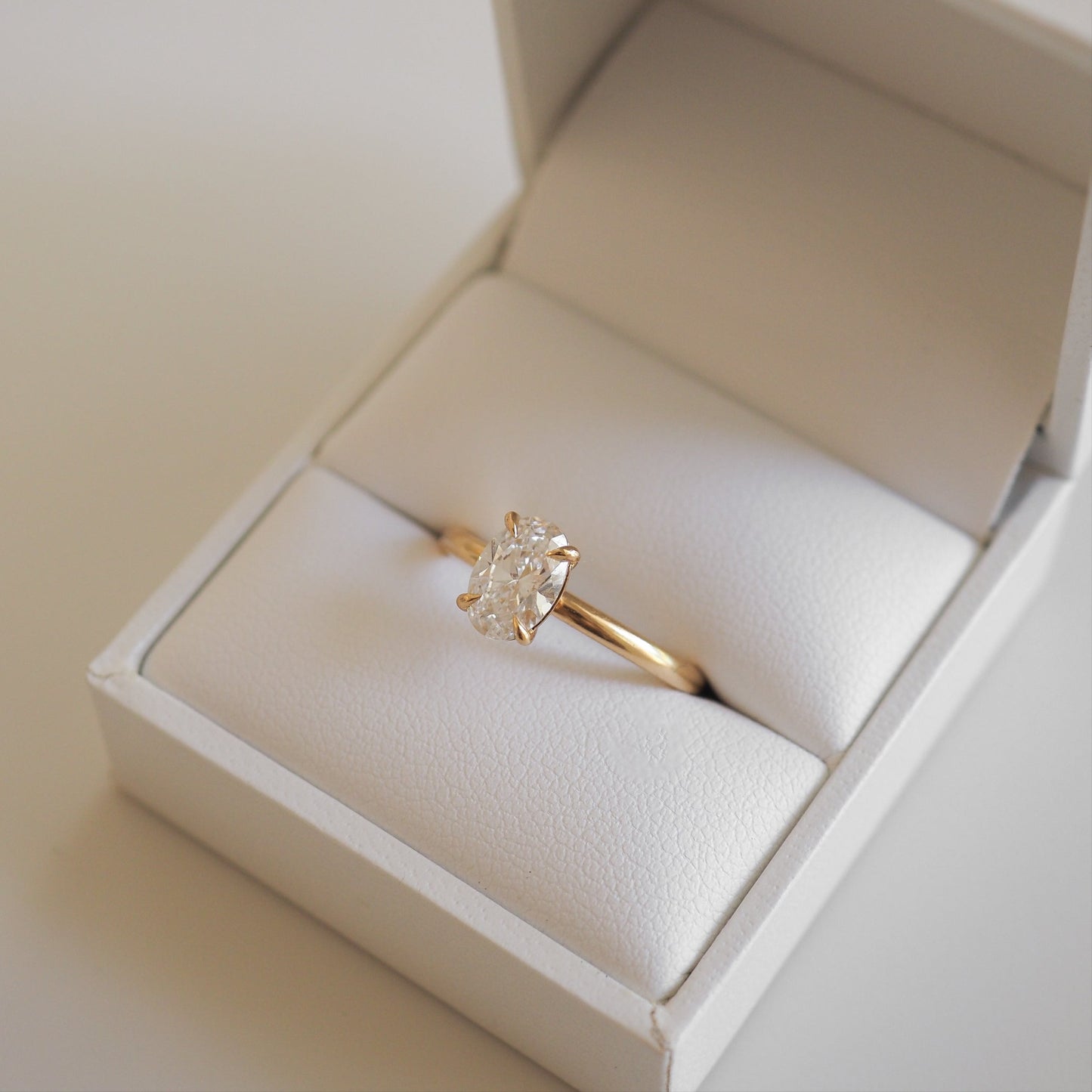 Gold engagement ring with a large oval diamond, elegantly displayed in a white jewellery box. Perfect luxury accessory for special occasions.