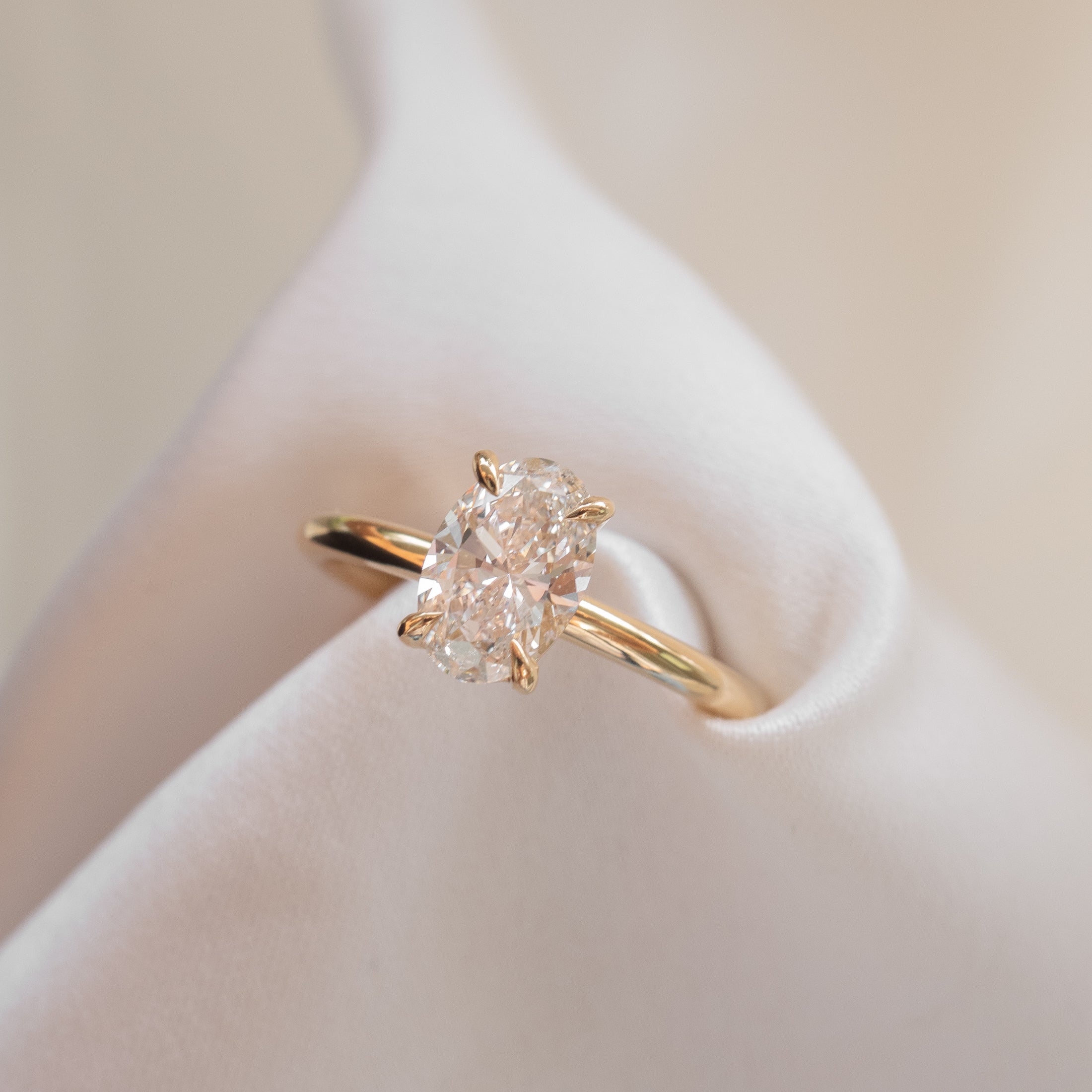 Oval diamond solitaire engagement ring set in a sleek yellow gold band, elegantly displayed on soft white fabric.
