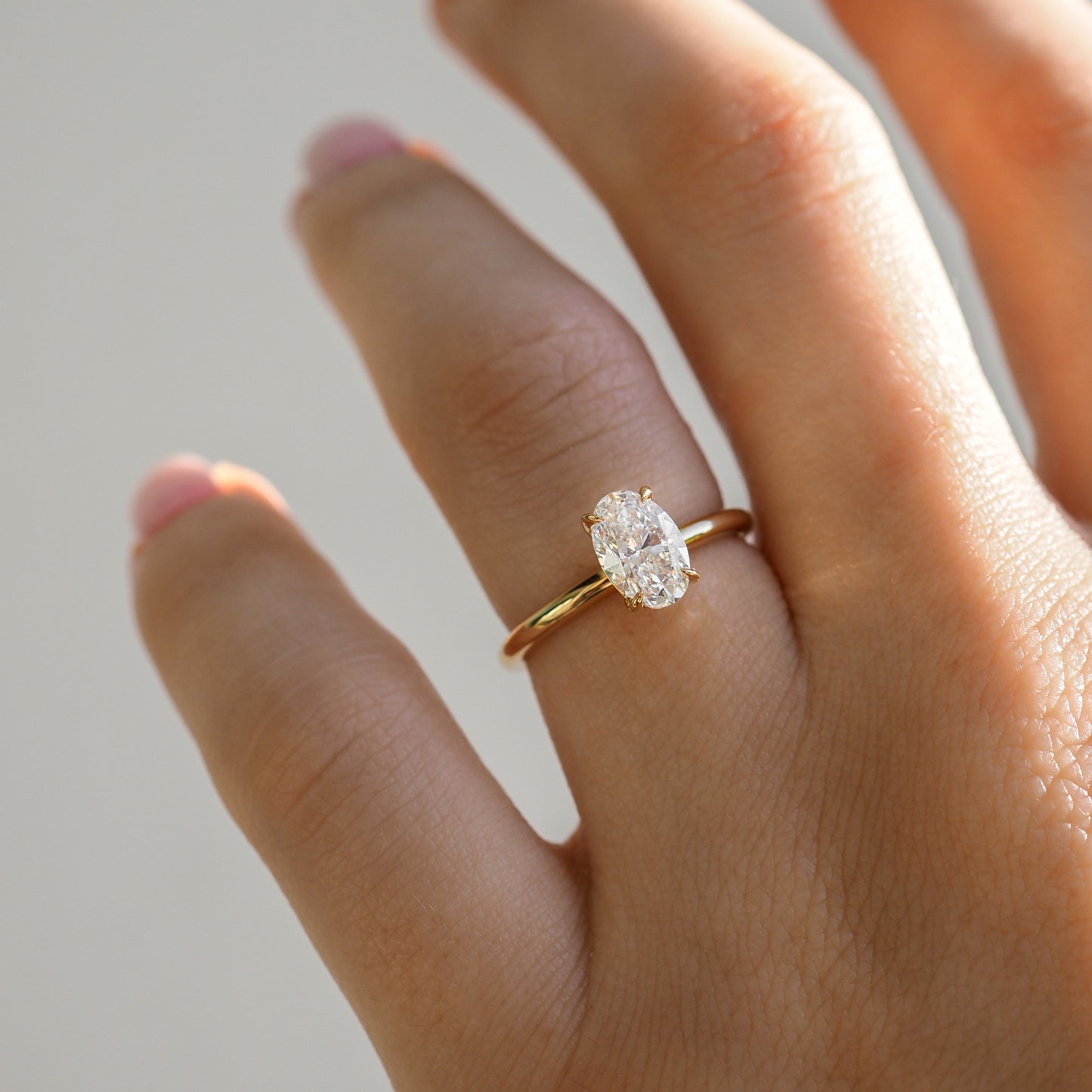 Gold band with an oval diamond ring on a hand. The ring glimmers in soft light, highlighting its elegant and luxurious design.