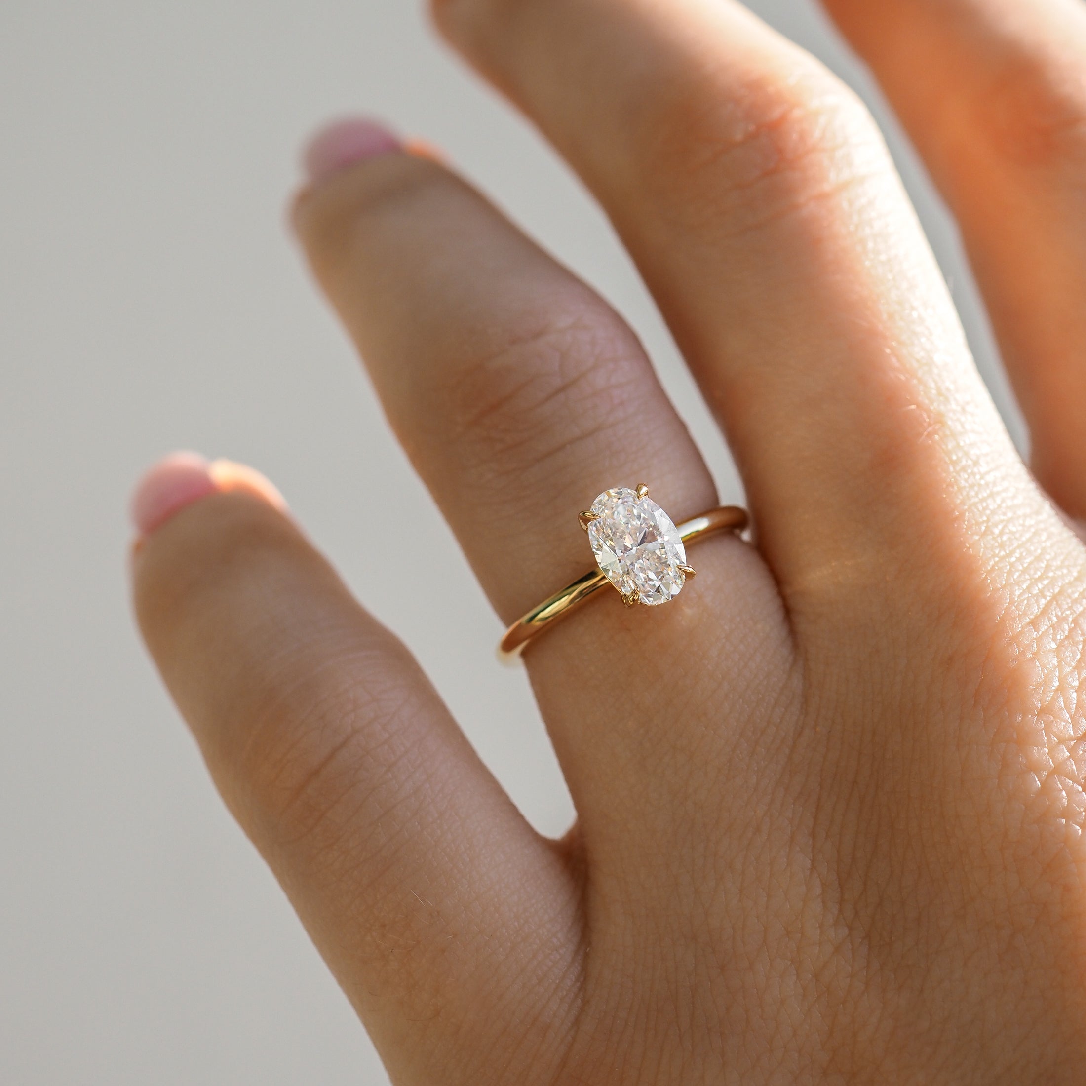 Gold band with an oval diamond ring on a hand. The ring glimmers in soft light, highlighting its elegant and luxurious design.