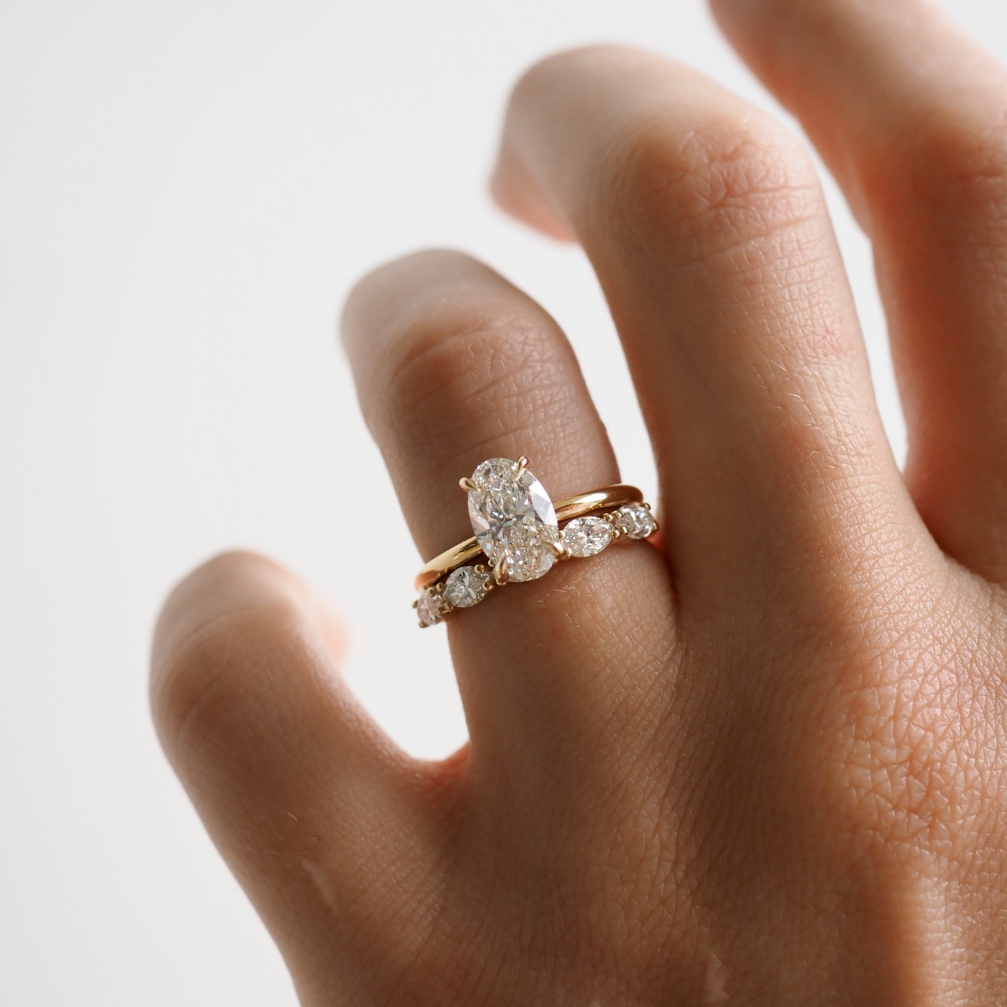 A hand wearing an elegant gold wedding band set, featuring an oval-cut diamond engagement ring and a diamond eternity band. Luxurious jewellery.