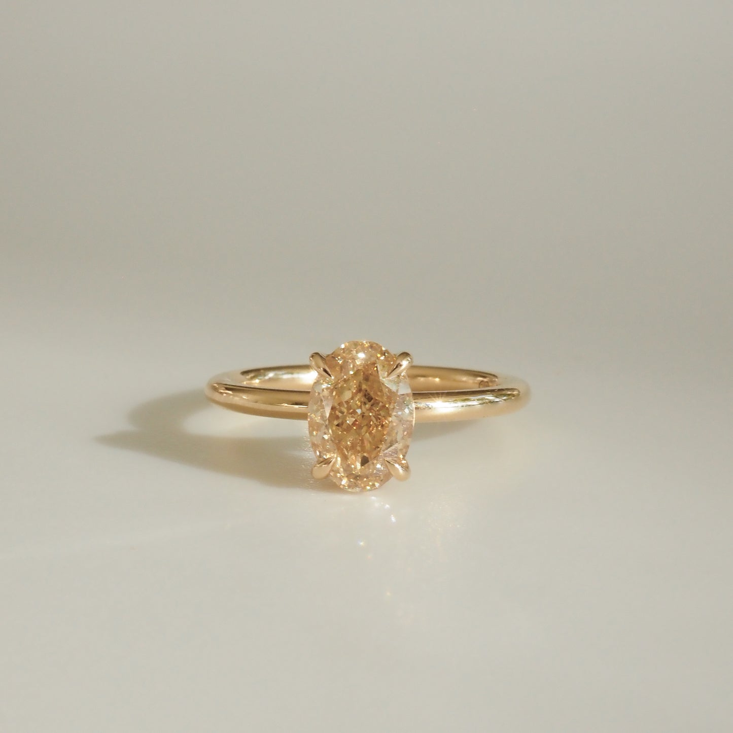 Elegant gold ring with an oval-cut yellow diamond centred on a minimalist band, showcased on a light background.