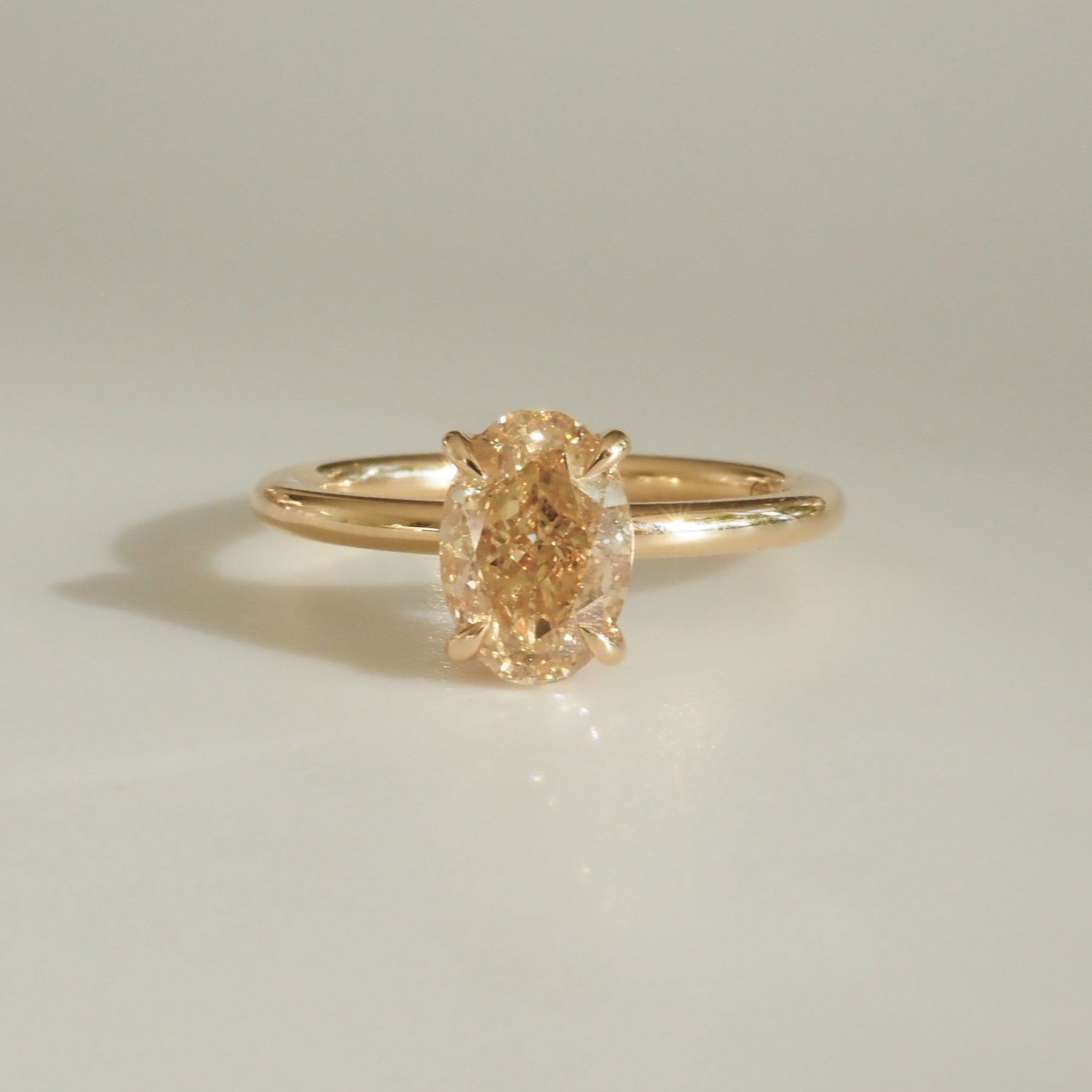 Elegant gold ring with an oval-cut yellow diamond centred on a minimalist band, showcased on a light background.