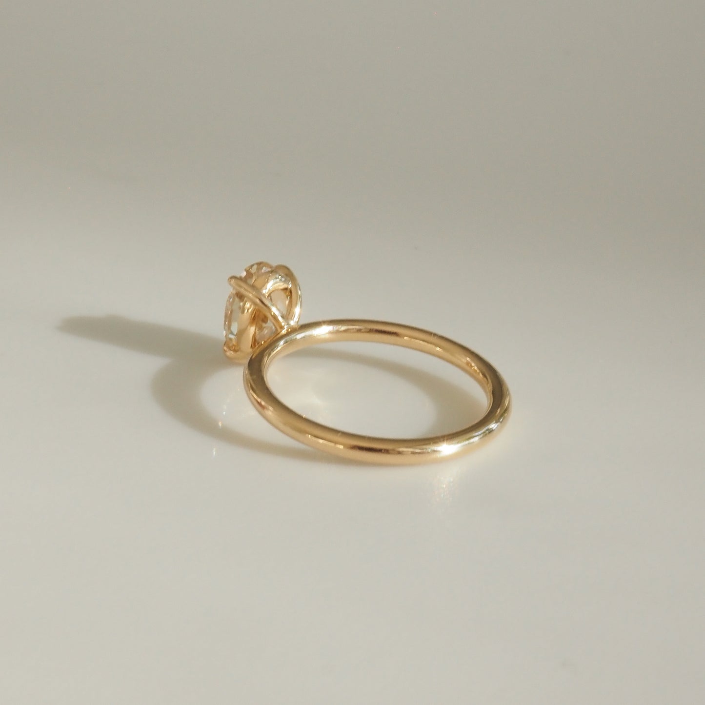 Elegant gold solitaire ring with a single diamond set on a smooth band, photographed on a soft, neutral background.