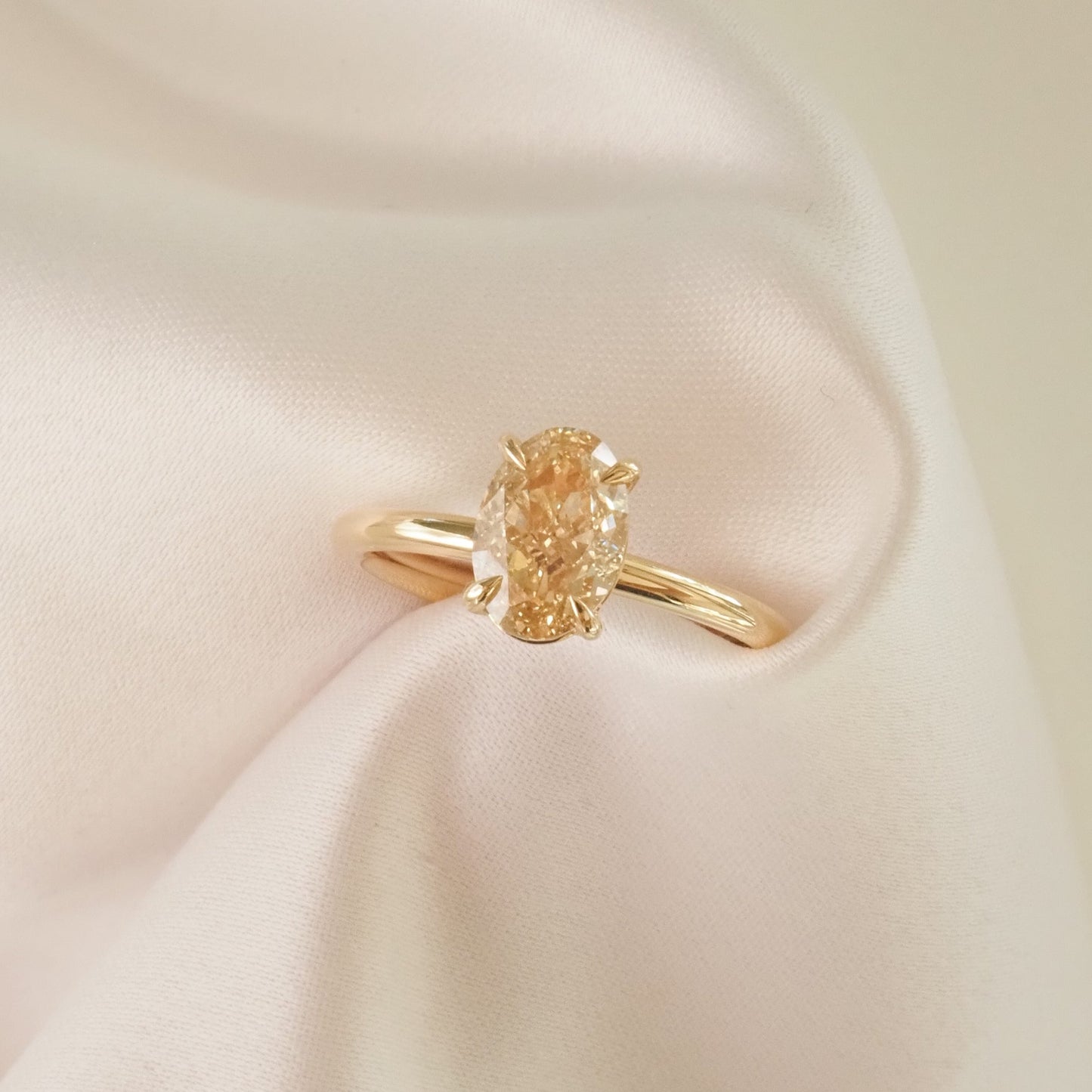 Gold ring with an oval-cut yellow diamond, elegantly displayed on soft, white fabric, highlighting its luxury and elegance in jewellery design.