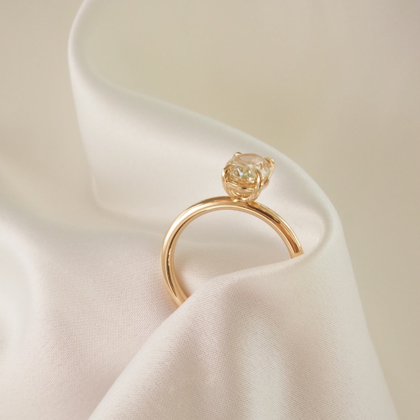 Gold engagement ring with solitaire diamond resting on luxurious white fabric. High-end jewellery, elegant and sophisticated design.