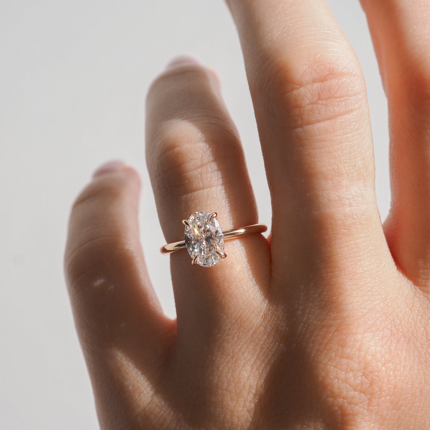 A hand wearing a gold ring with a large, oval-cut diamond. The background is softly lit, highlighting the luxury jewellery piece.