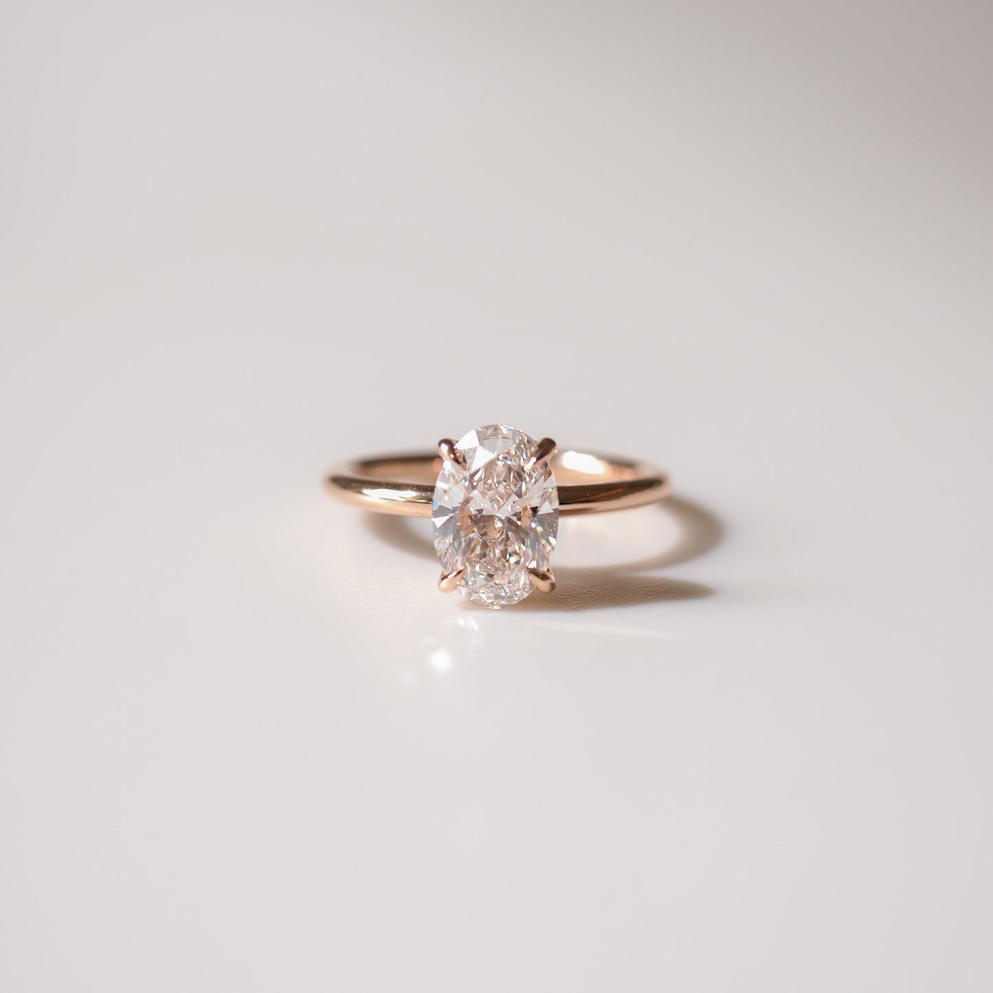 Oval diamond ring with gold band on white surface; elegant, minimalistic design. Perfect for luxury jewellery enthusiasts.