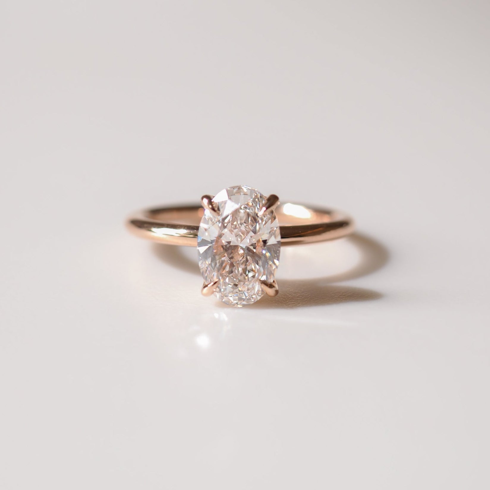 Oval diamond ring with gold band on white surface; elegant, minimalistic design. Perfect for luxury jewellery enthusiasts.