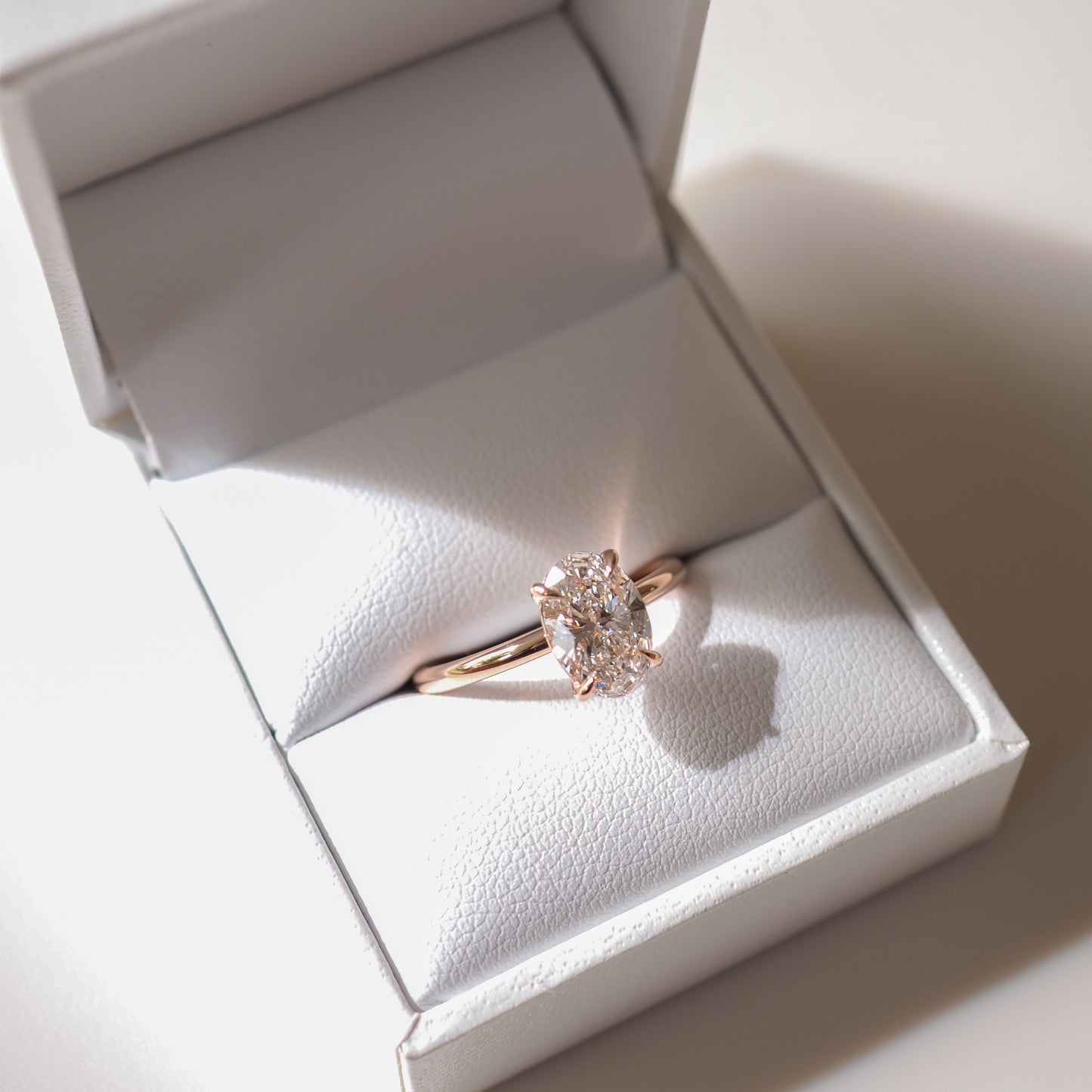 Rose gold engagement ring with an oval diamond set in a white jewellery box, showcasing luxury craftsmanship and elegance.