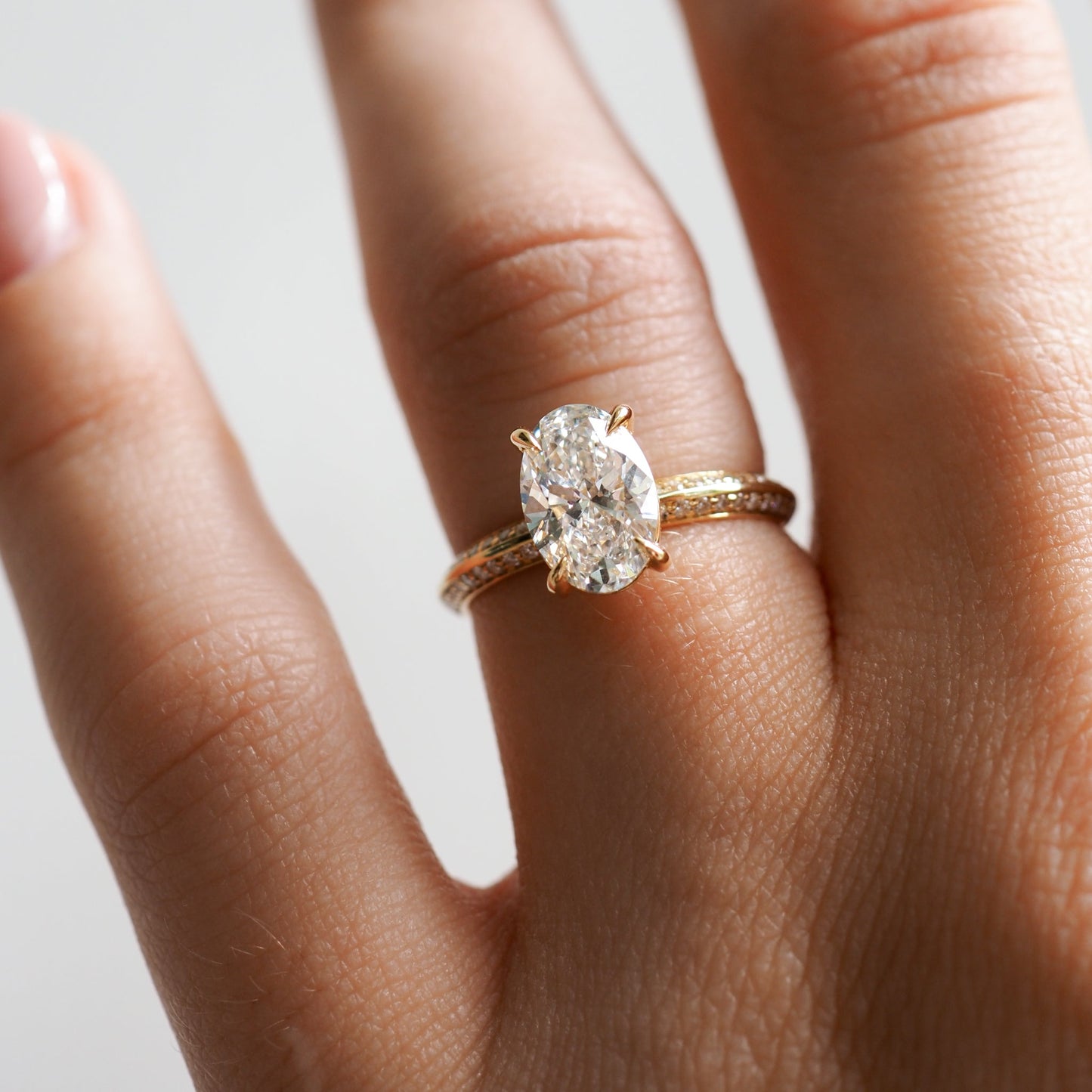 Close-up of a hand wearing an oval-cut diamond engagement ring and a textured yellow gold band, showcasing luxury jewellery elegance.