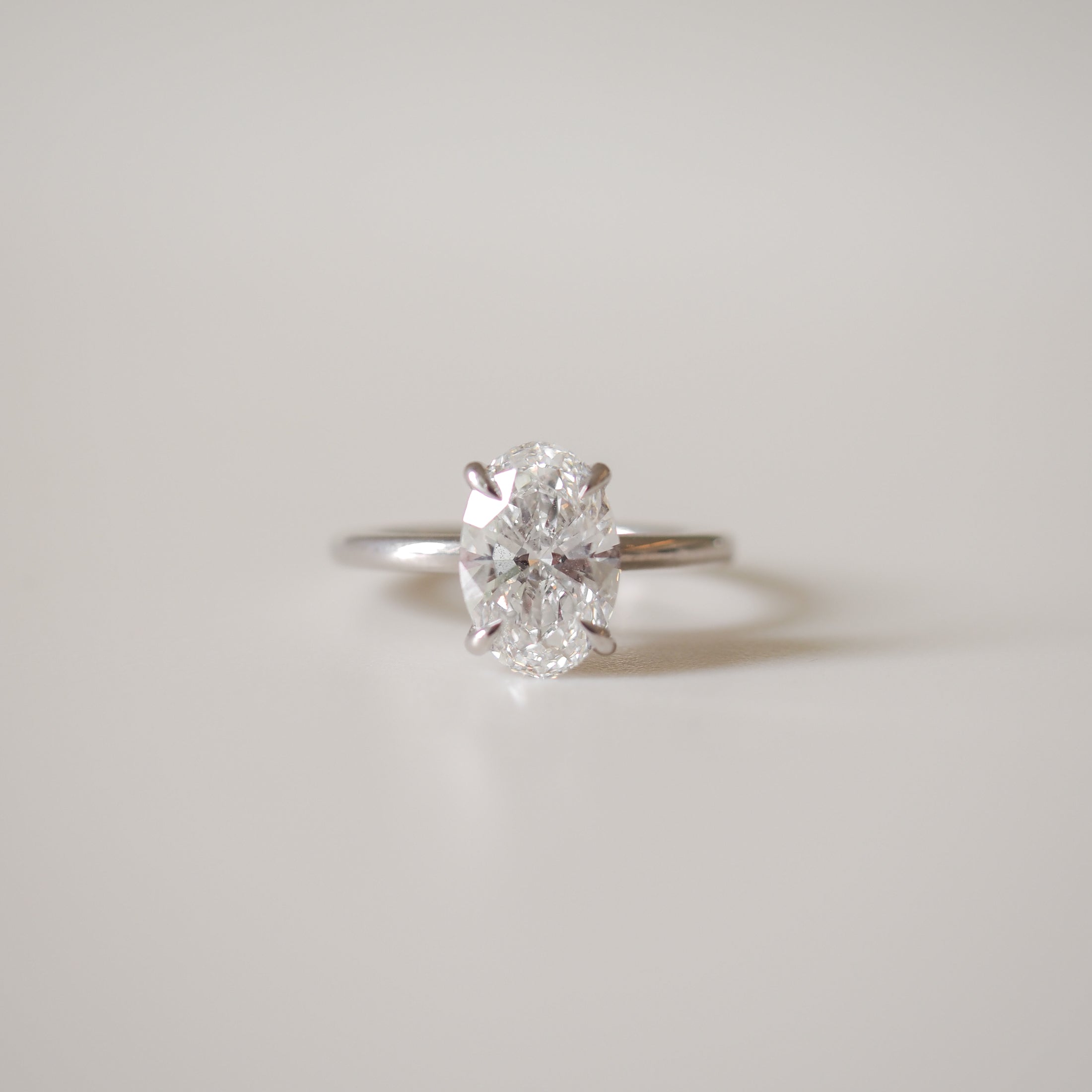 Oval-cut diamond ring with a simple white gold band, set against a soft grey background, showcasing luxury jewellery elegance.