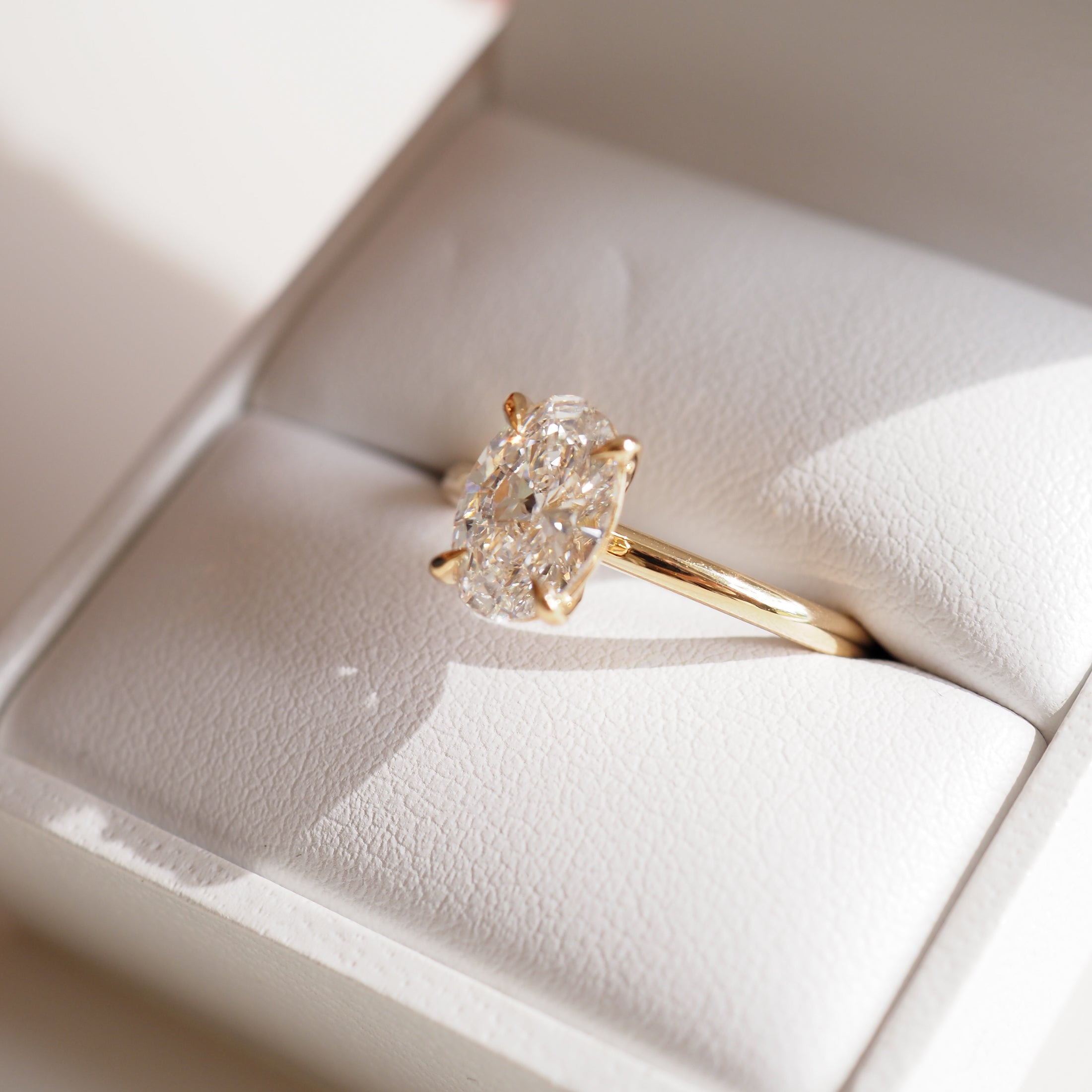Oval-cut diamond ring in a gold setting, displayed in a white jewellery box. Elegant and luxurious fine jewellery.