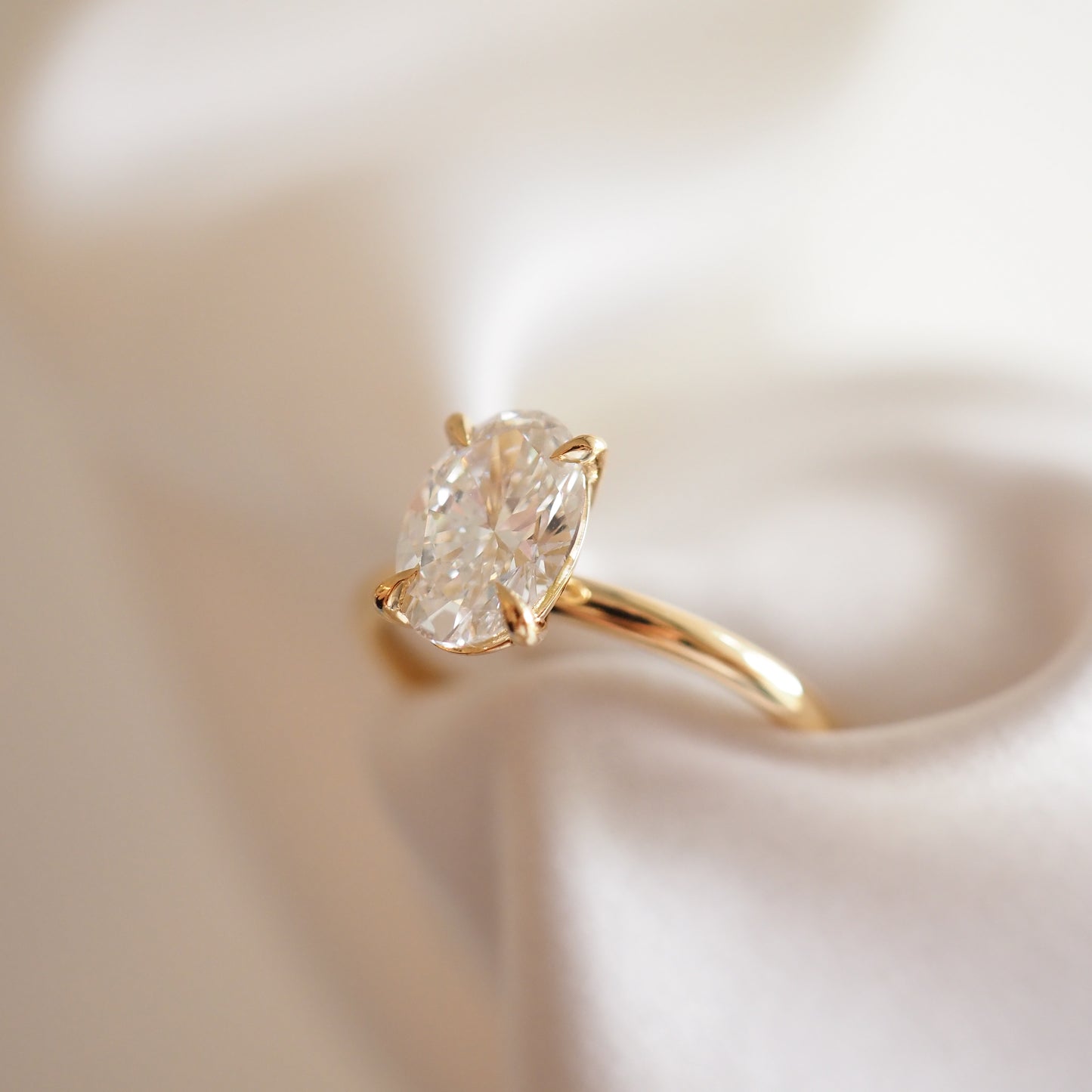 Elegant gold solitaire ring with an oval diamond, set against soft, luxurious white fabric, showcasing high-end jewellery in Australia.