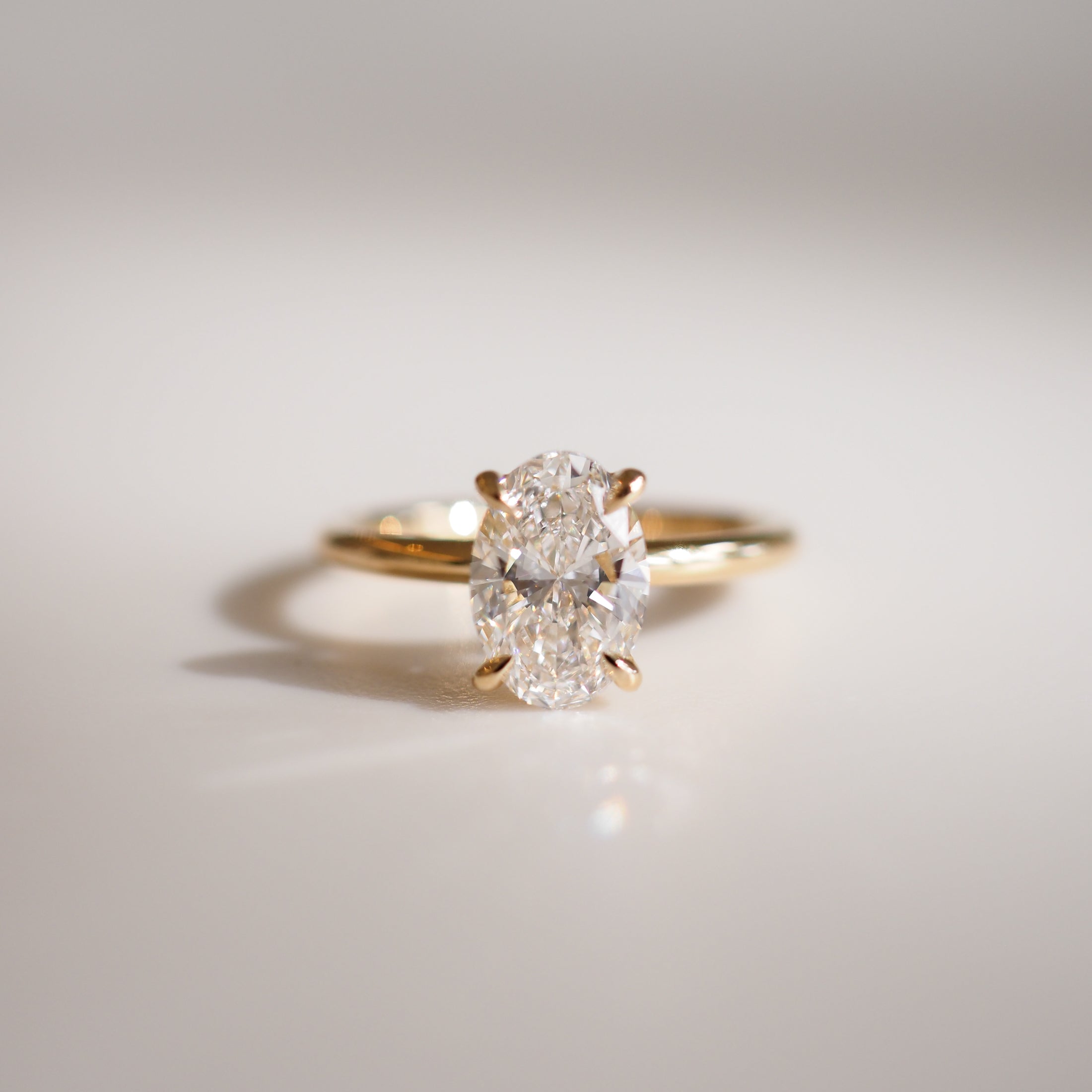 Elegant gold ring with an oval-cut diamond, casting a soft shadow on a pale surface, embodying luxury and sophistication in jewellery design.