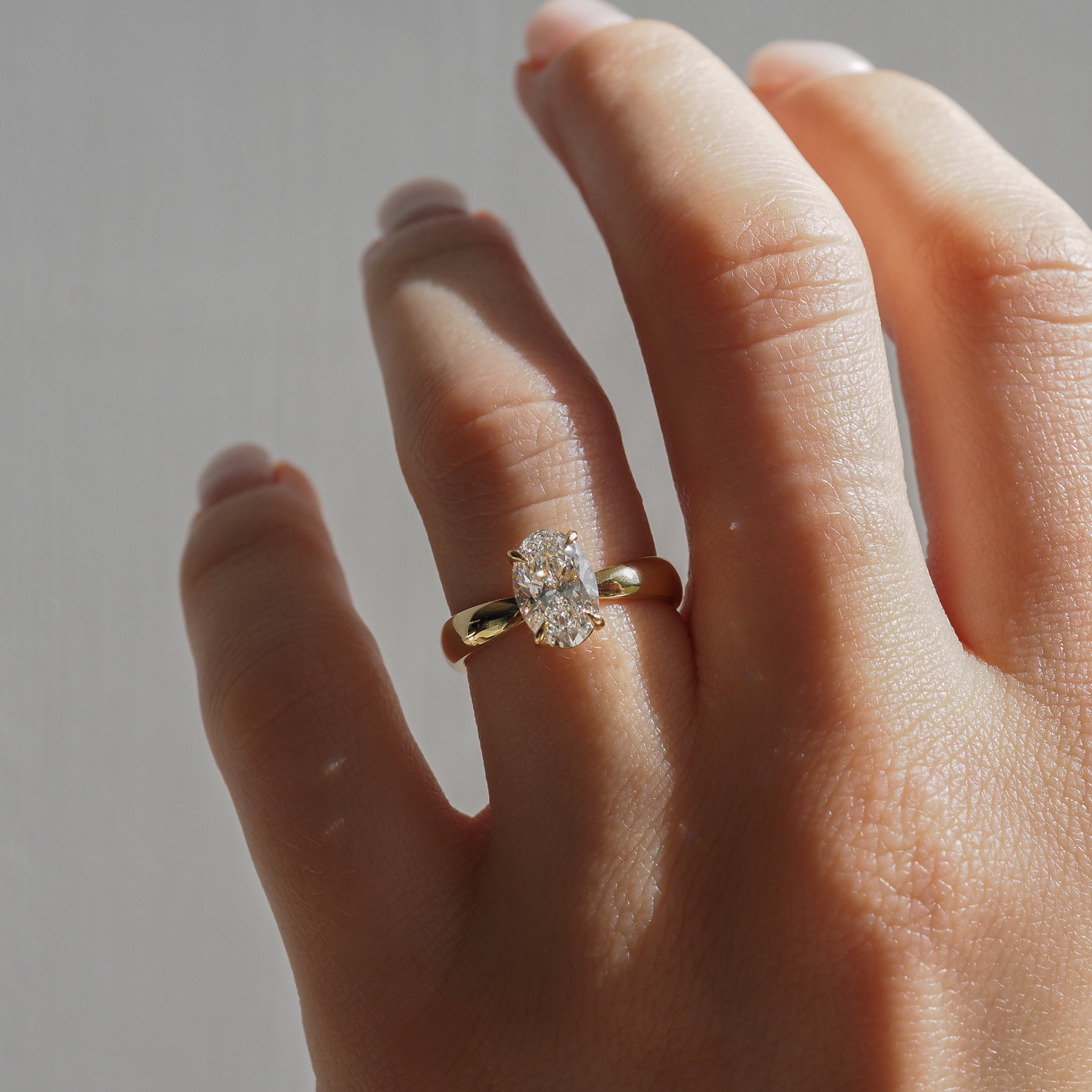 Hand displaying an elegant gold ring with a large oval diamond, capturing the essence of luxury jewellery under natural light.