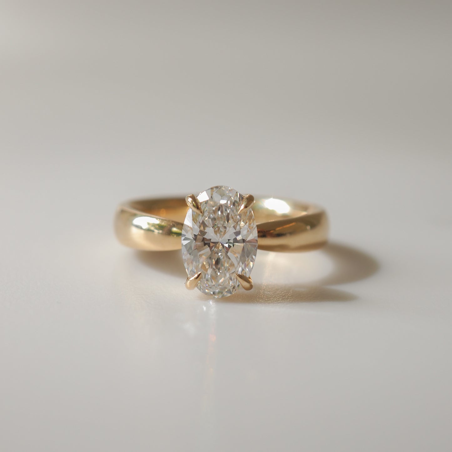Gold ring with an oval cut diamond solitaire, reflecting light on a neutral background. Ideal for luxury jewellery lovers.