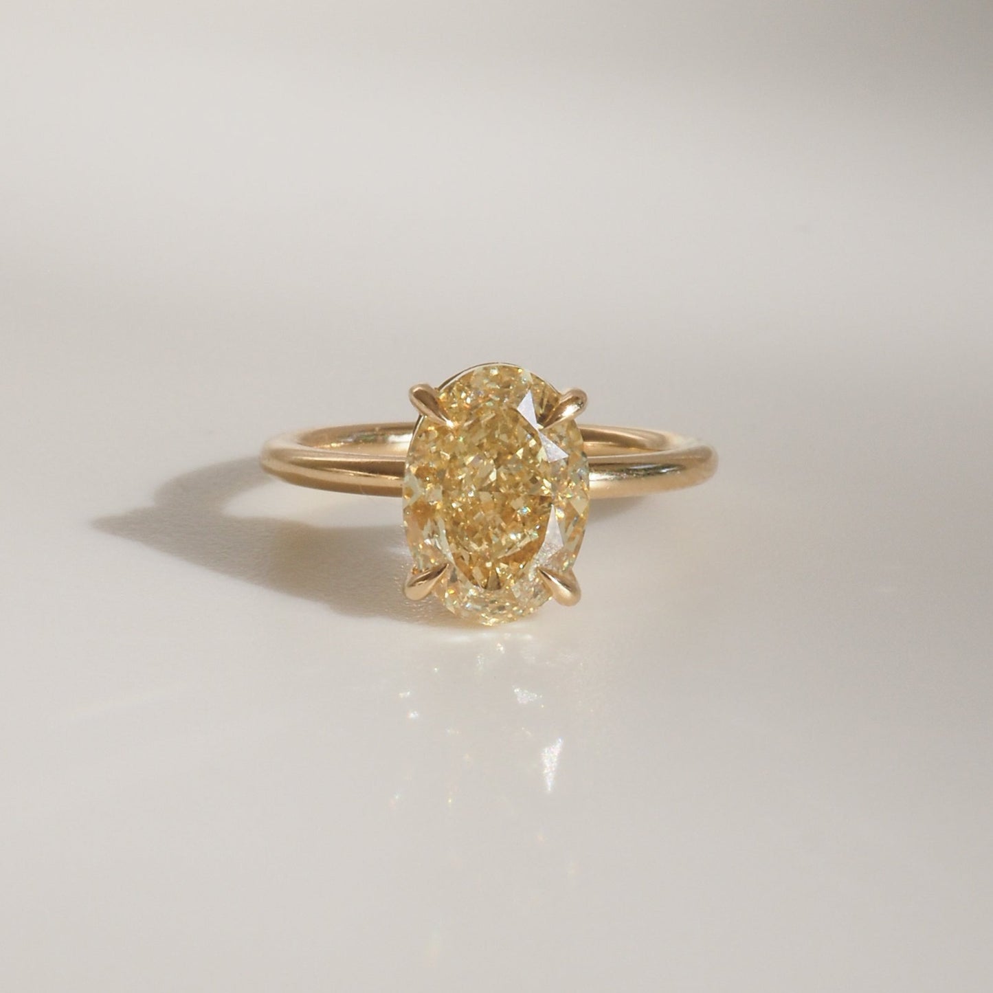 Elegant gold ring with a large oval yellow diamond, casting a soft shadow on a light background. Luxurious jewellery design.