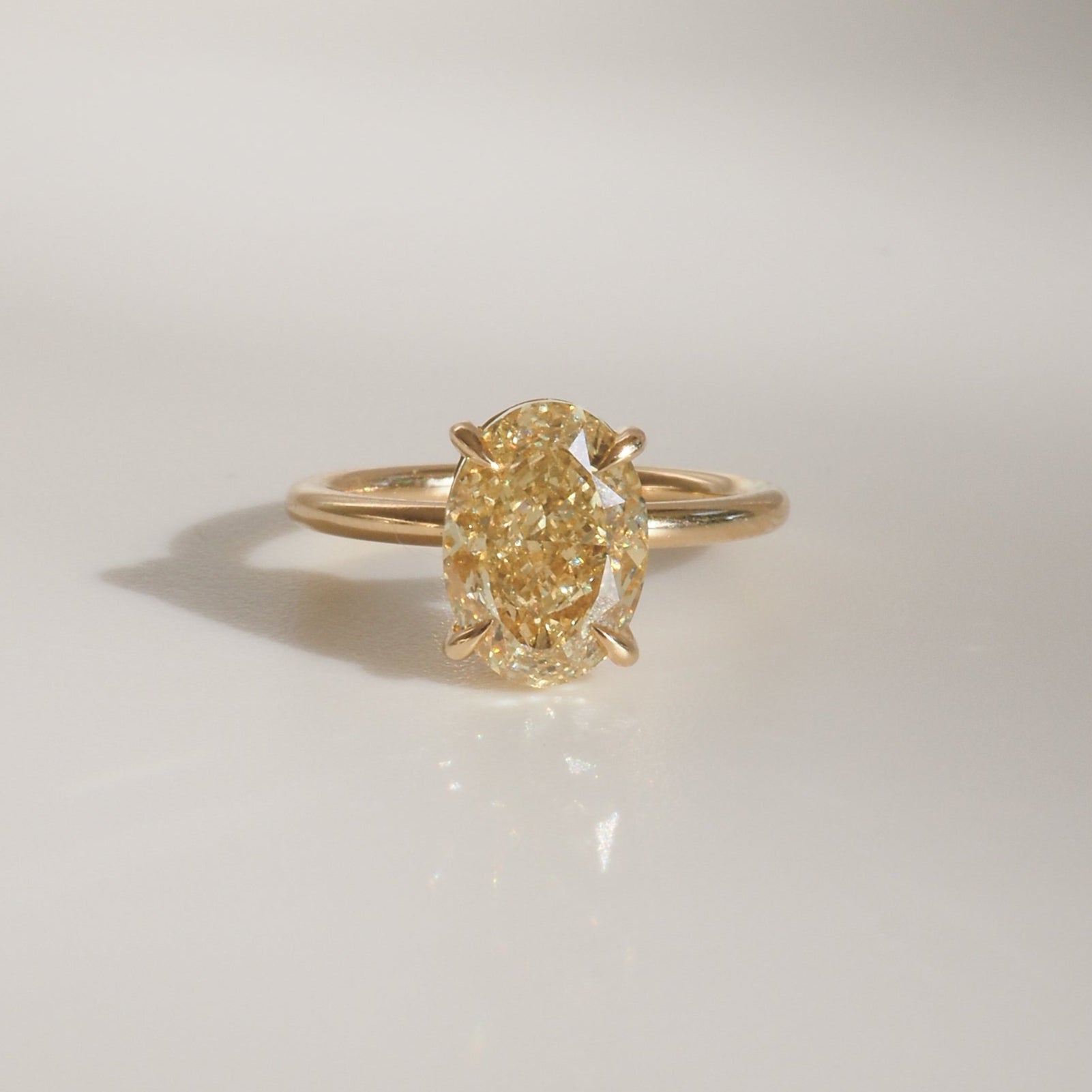 Elegant gold ring with a large oval yellow diamond, casting a soft shadow on a light background. Luxurious jewellery design.