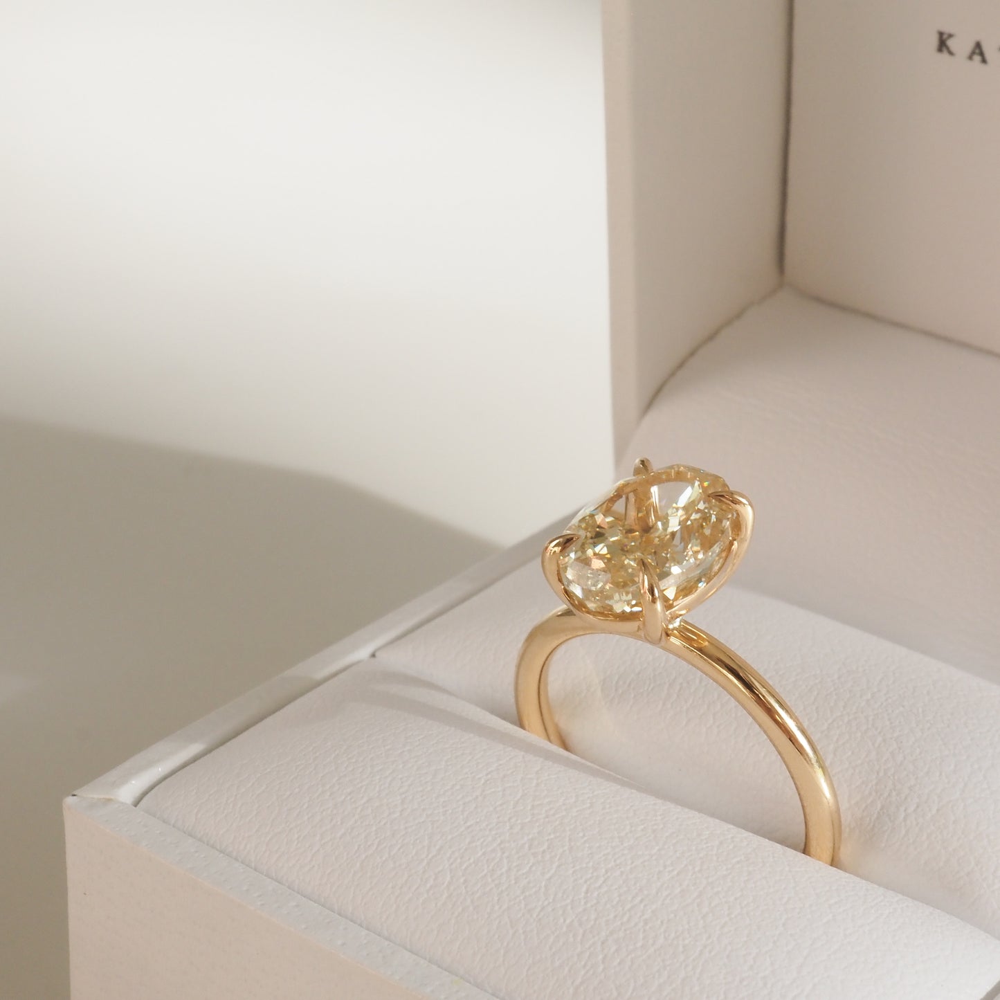 Elegant gold ring with a prominent oval yellow diamond set in a white jewellery box, perfect for luxury engagement or wedding occasions.