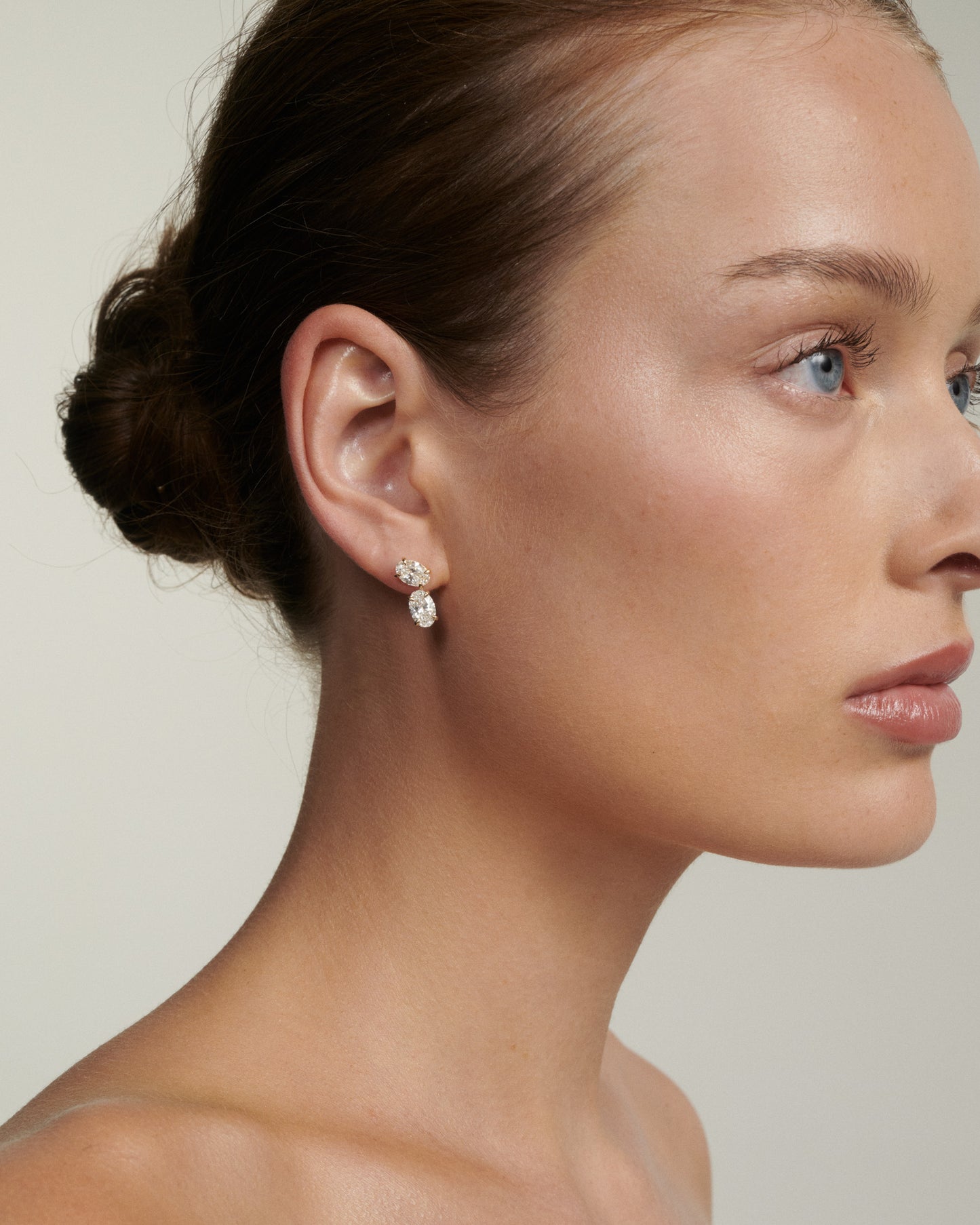 Close-up of a woman wearing diamond earrings against a neutral background