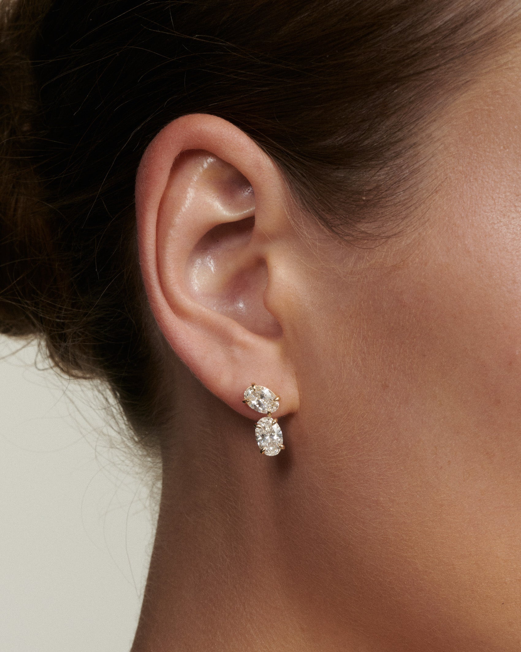 Close-up of an ear wearing a diamond earring with a neutral background