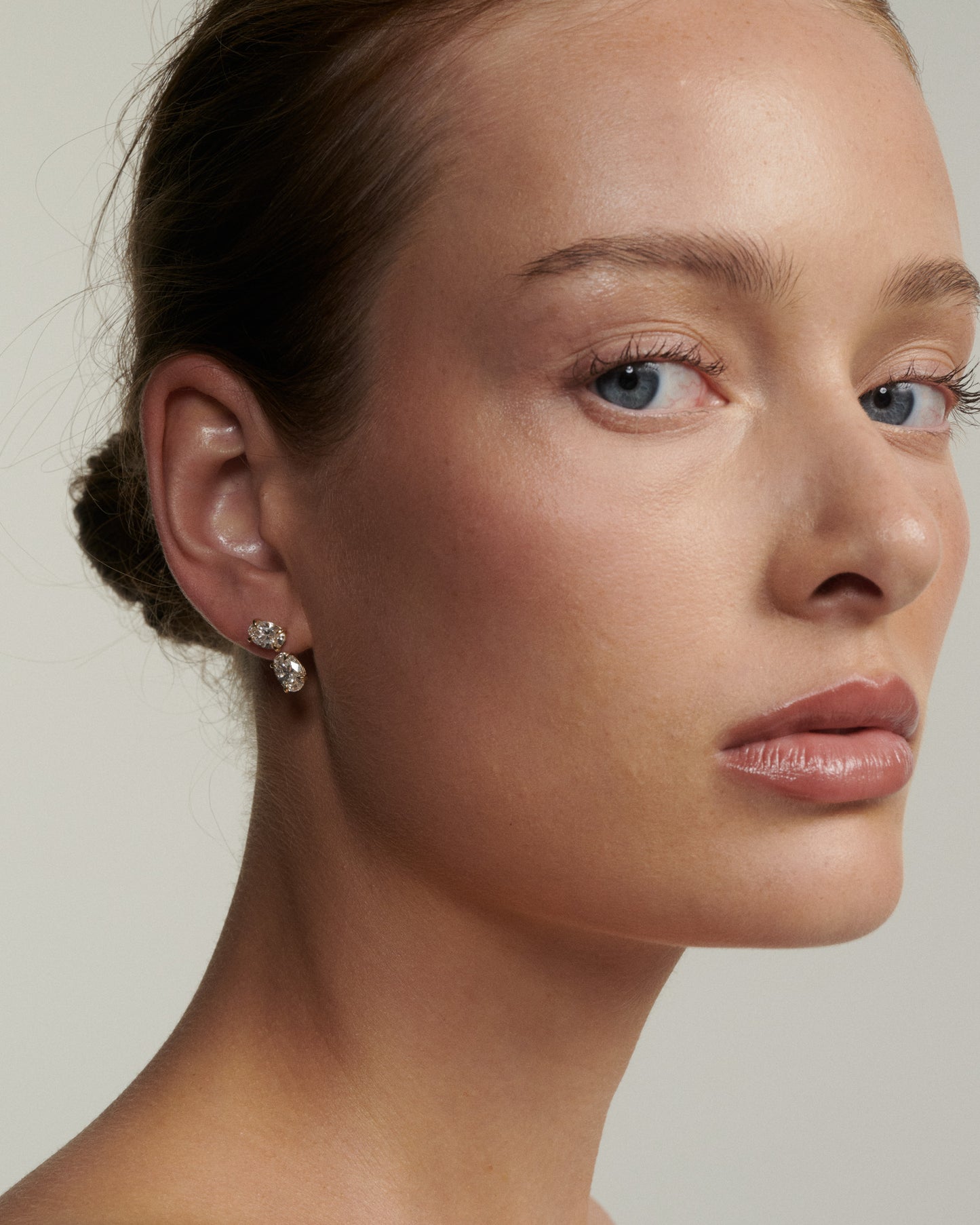 Close-up of a woman wearing diamond earrings against a neutral background