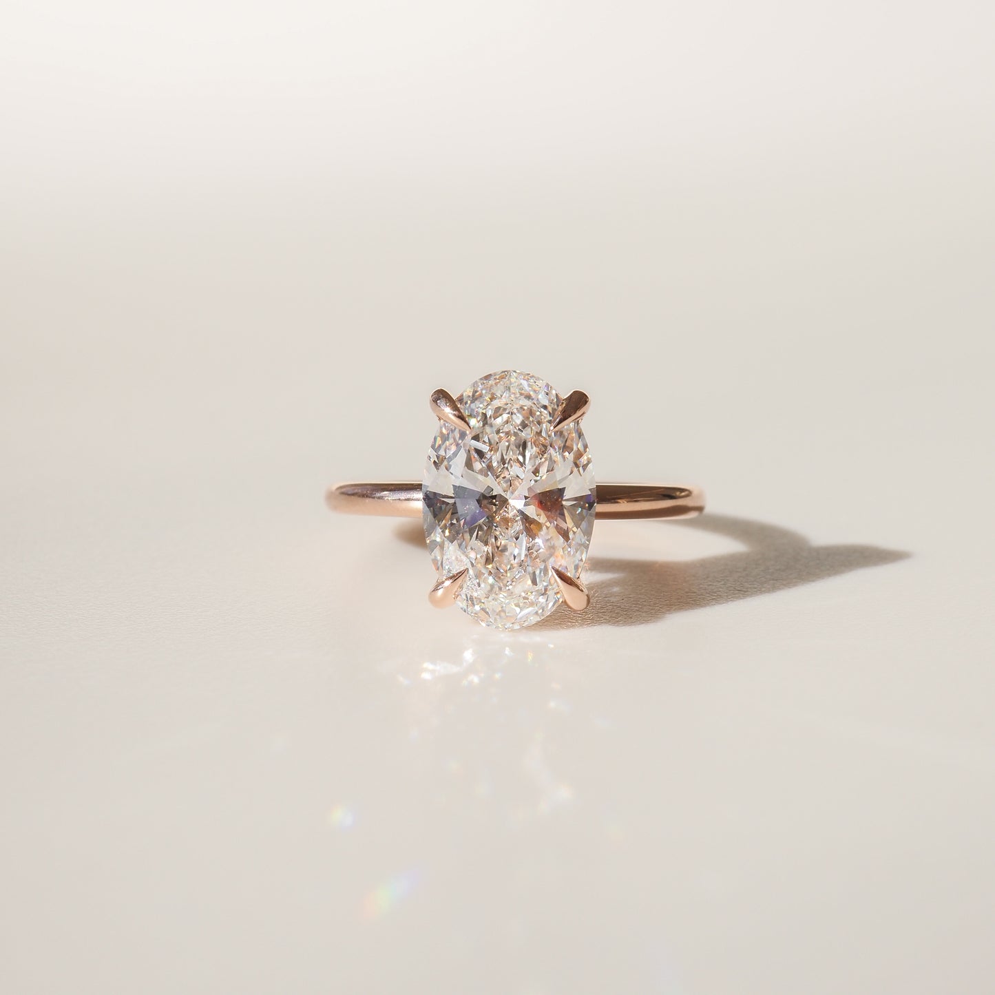Oval diamond ring with a rose gold band, sparkling under soft light, casting a delicate shadow on a neutral background.