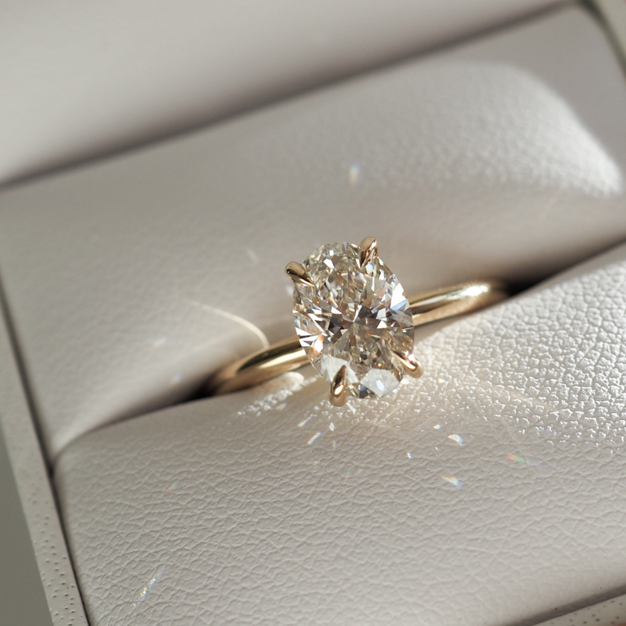 Oval diamond ring in a gold setting, elegantly displayed in a white jewellery box, reflecting light to create a sparkling effect.