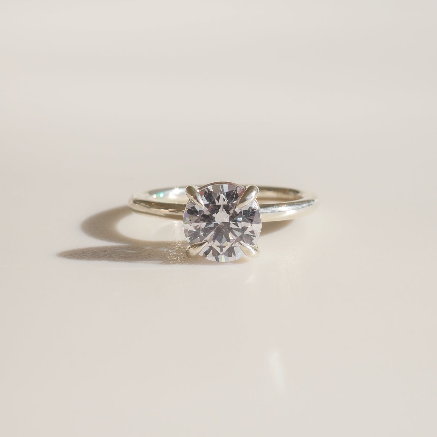 Diamond solitaire engagement ring with a brilliant-cut gem on a sleek silver band, set against a soft, light background. Luxurious jewellery.