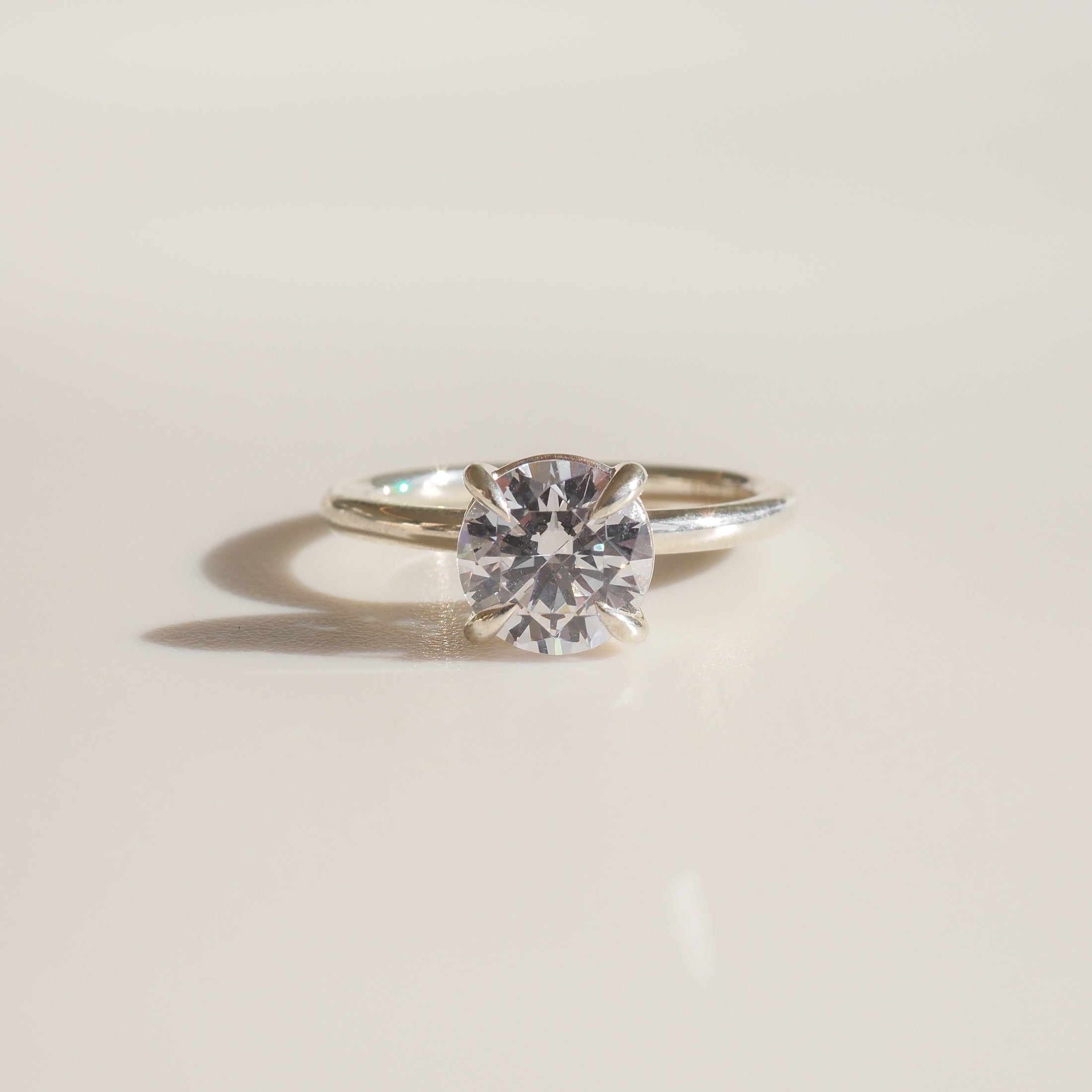Diamond solitaire engagement ring with a brilliant-cut gem on a sleek silver band, set against a soft, light background. Luxurious jewellery.