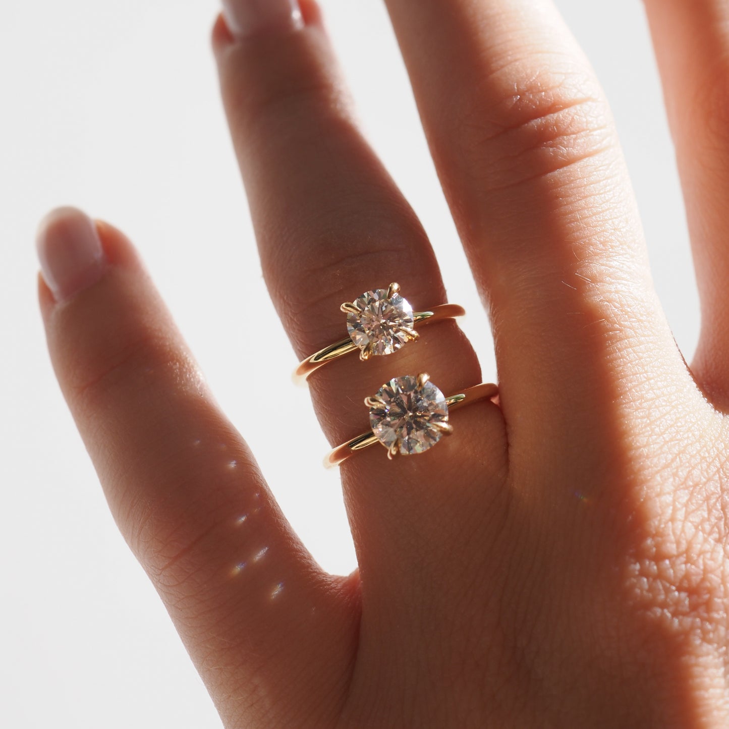 Hand wearing two gold rings with large round diamonds, elegantly displayed against a soft-lit background. Perfect for luxury jewellery lovers.