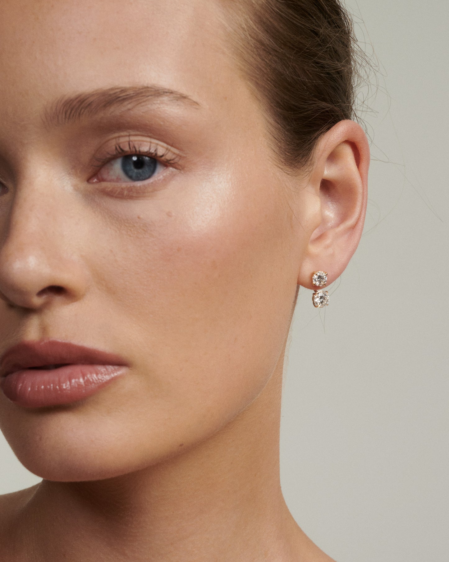 Close-up of a woman wearing diamond earrings on a neutral background