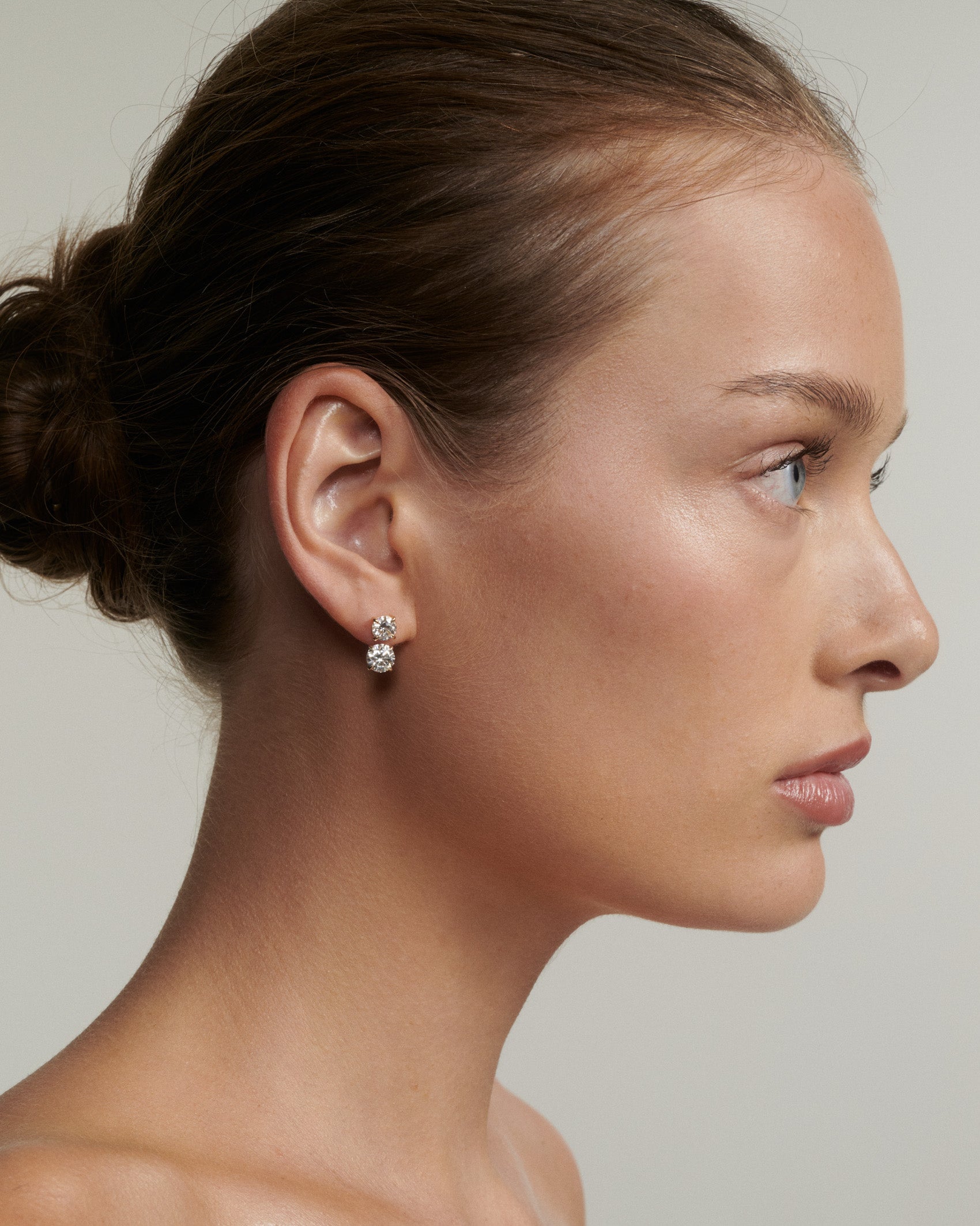 Side profile of a woman wearing a diamond earring against a neutral background