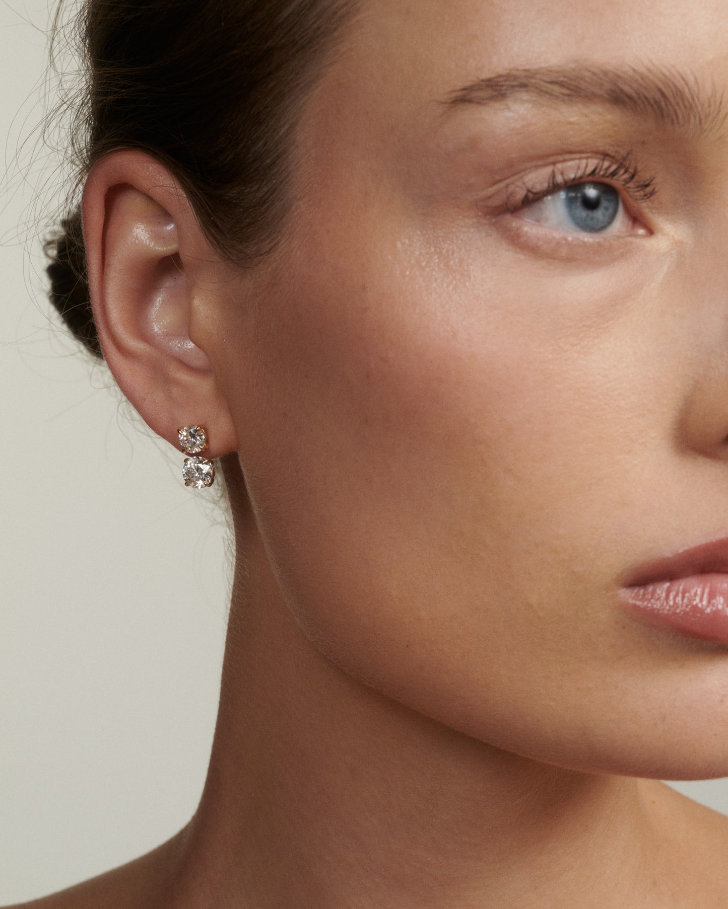 Close-up of a woman wearing diamond earrings with a neutral background