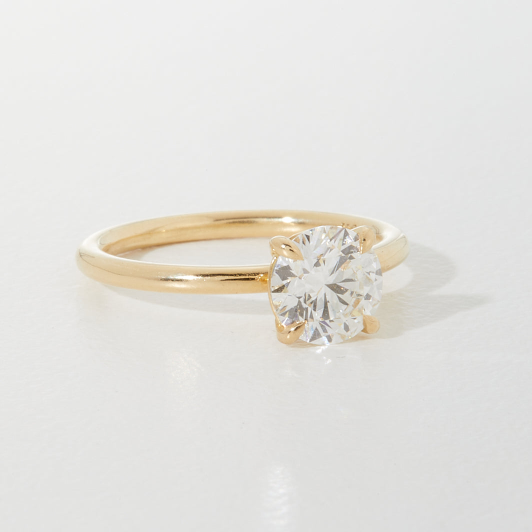Gold engagement ring with a solitaire diamond set in classic prongs on a polished band, displayed on a light background.