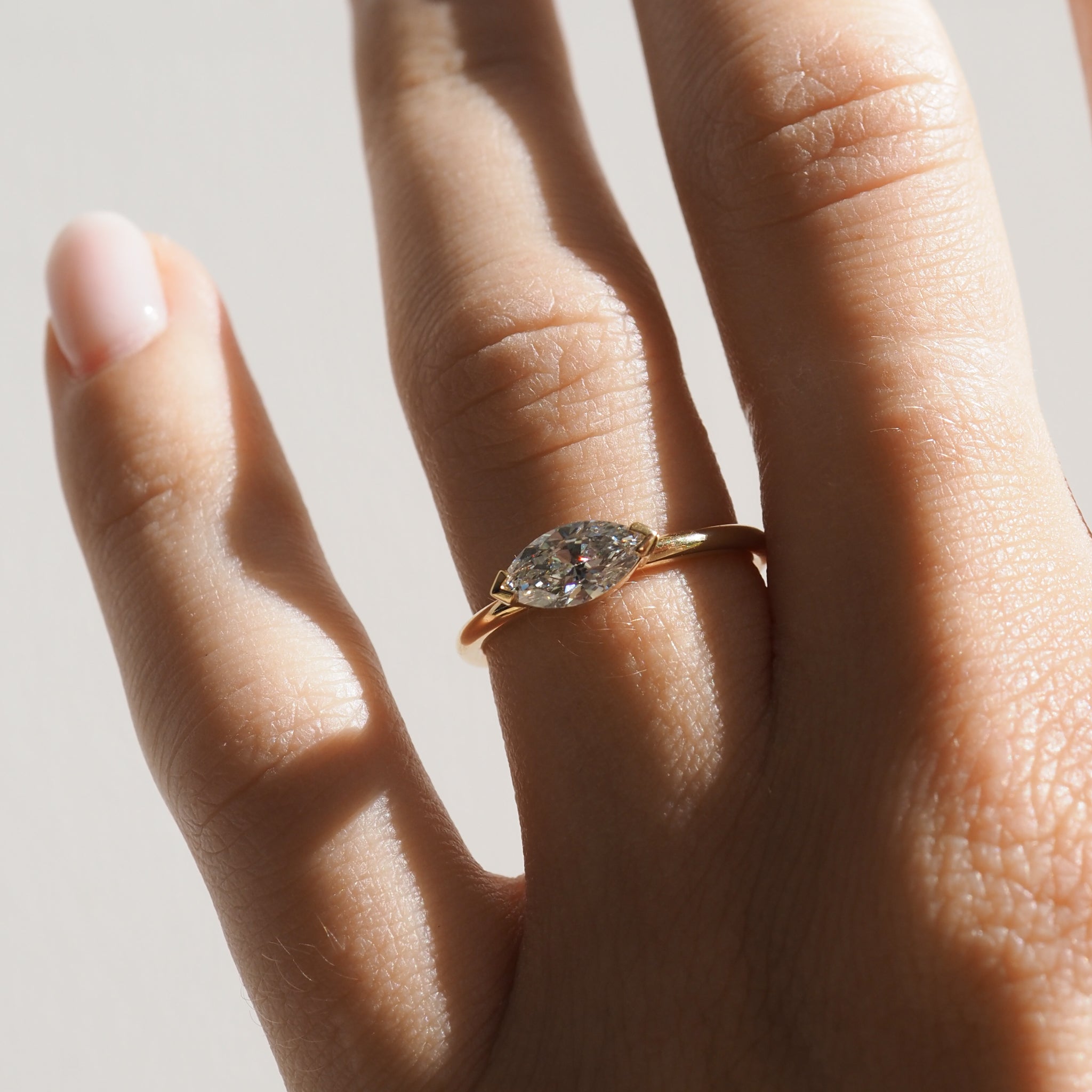 Close-up of a hand wearing a marquise-cut diamond ring with a gold band, showcasing luxury jewellery in natural light.
