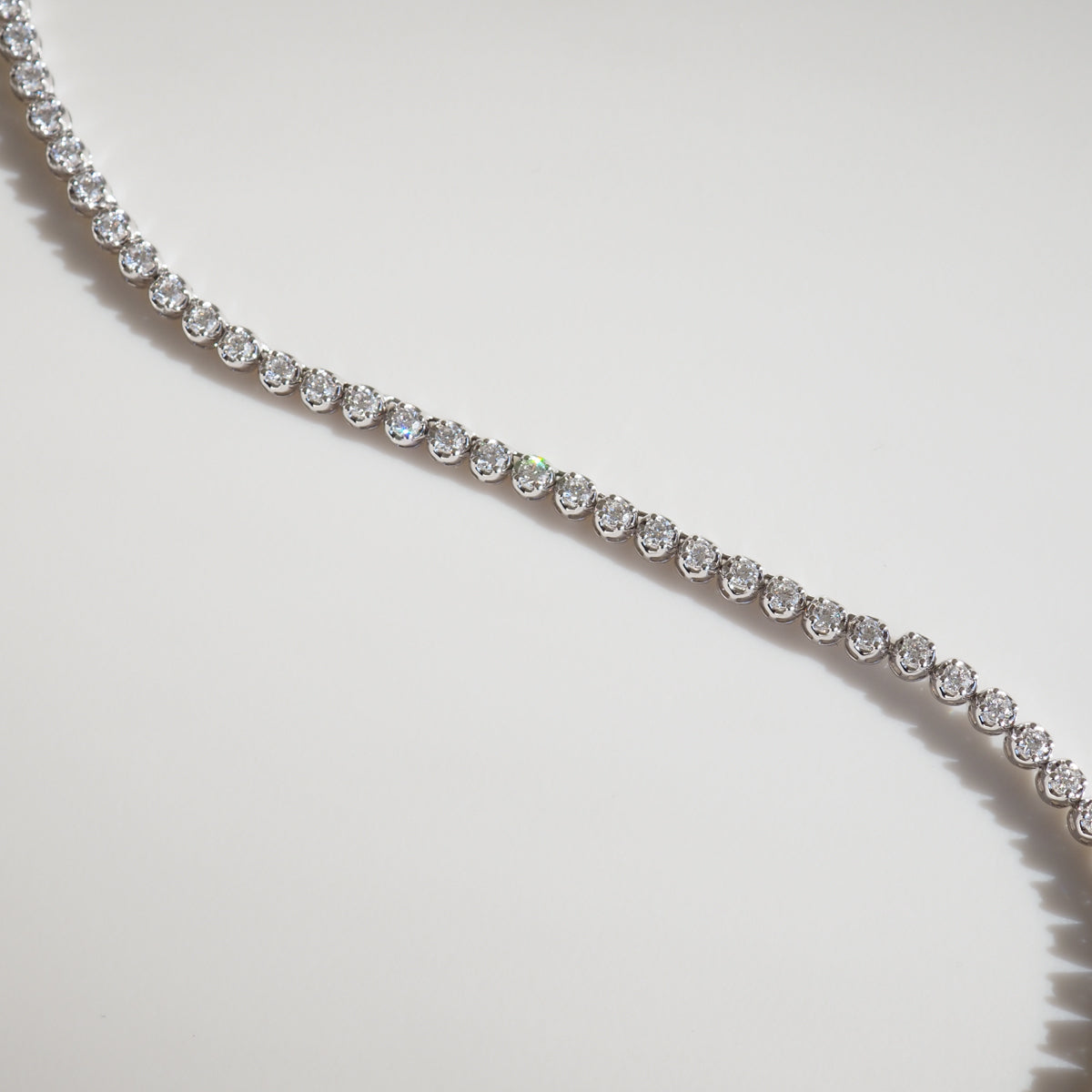 Elegant diamond tennis bracelet with sparkling round stones set in a thin gold band, displayed on a soft white background.