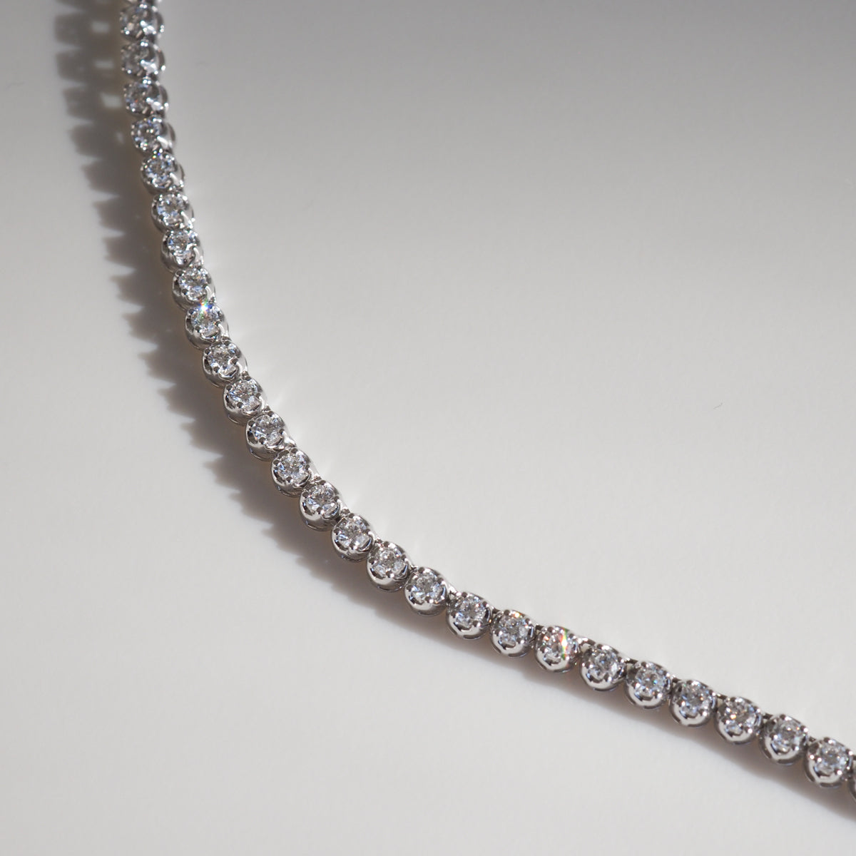 Elegant diamond tennis necklace with sparkling round stones in a single row, set in platinum, displayed on a plain background.