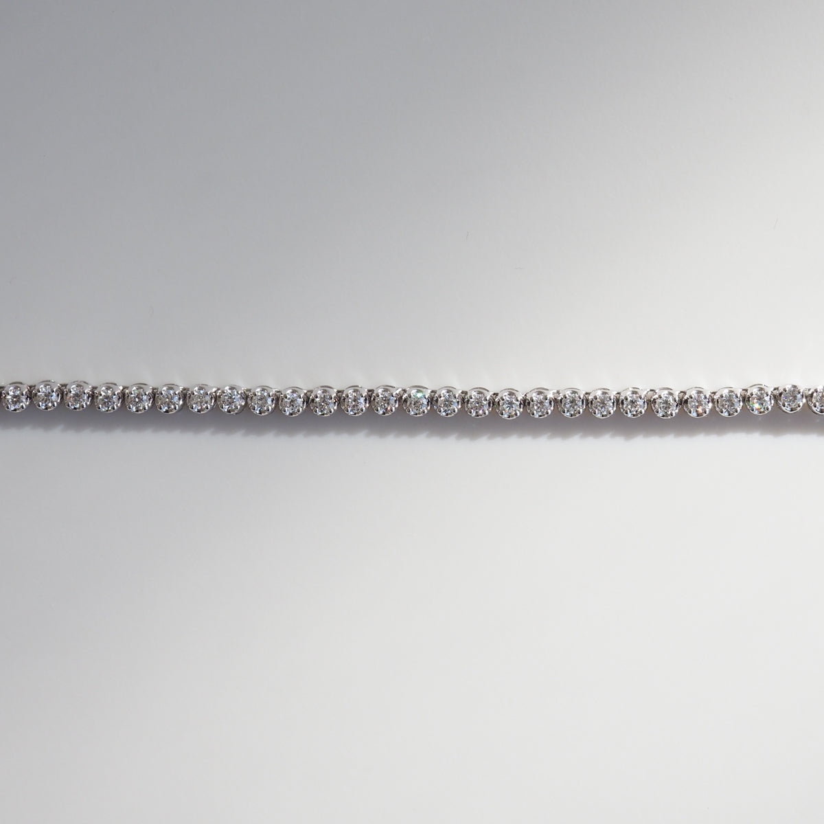 Elegant diamond tennis bracelet with sparkling round stones, set in white gold, displayed against a soft gradient background.