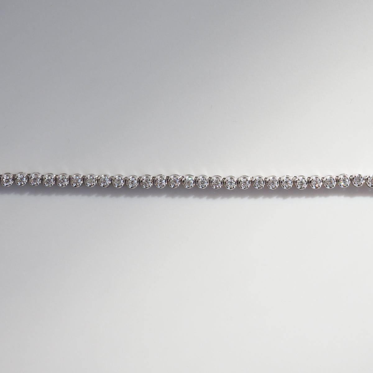 Elegant diamond tennis bracelet set in white gold, beautifully reflecting light against a soft grey background. Perfect example of luxury jewellery.
