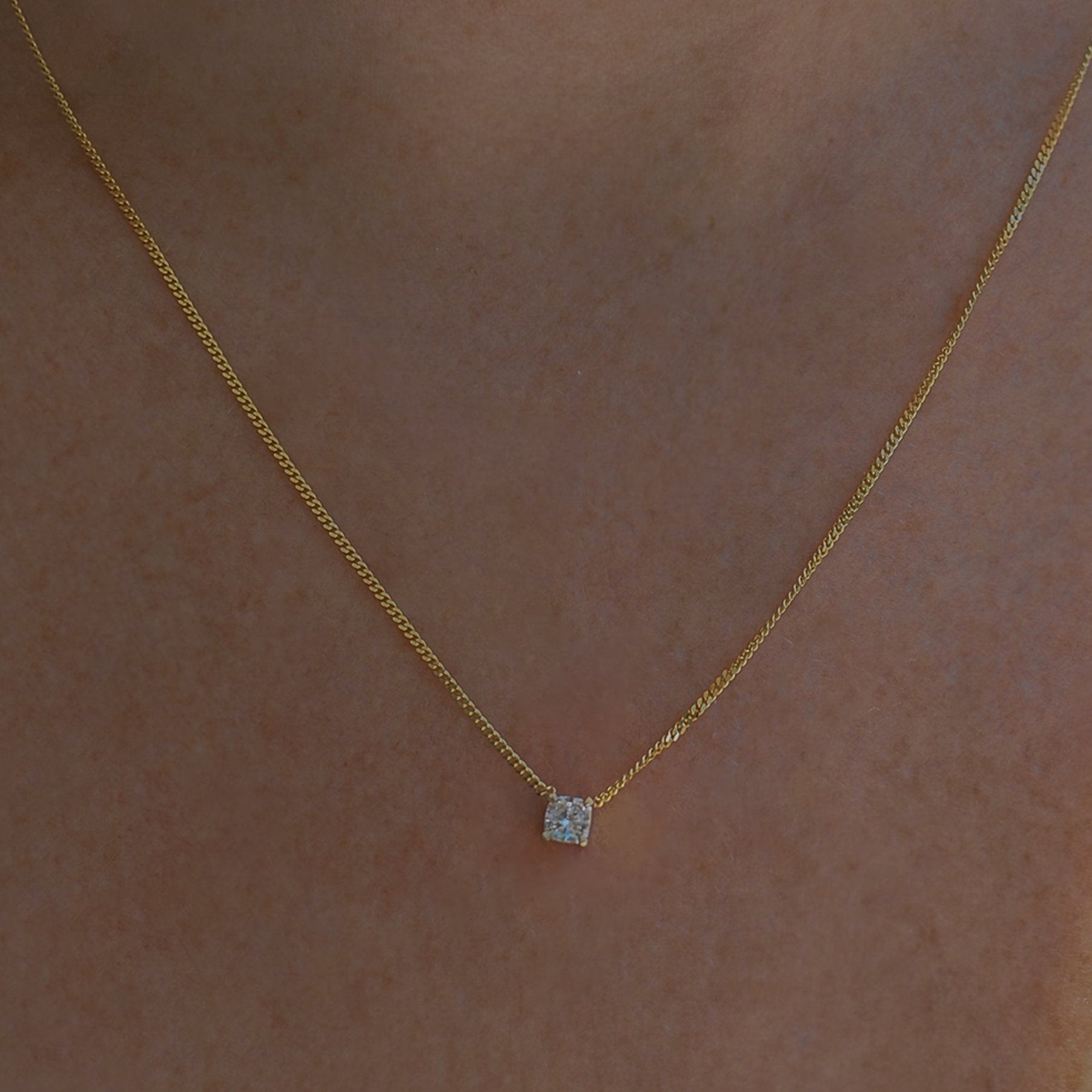Gold necklace with a delicate chain and a small, square diamond pendant, elegantly resting on a skin backdrop.