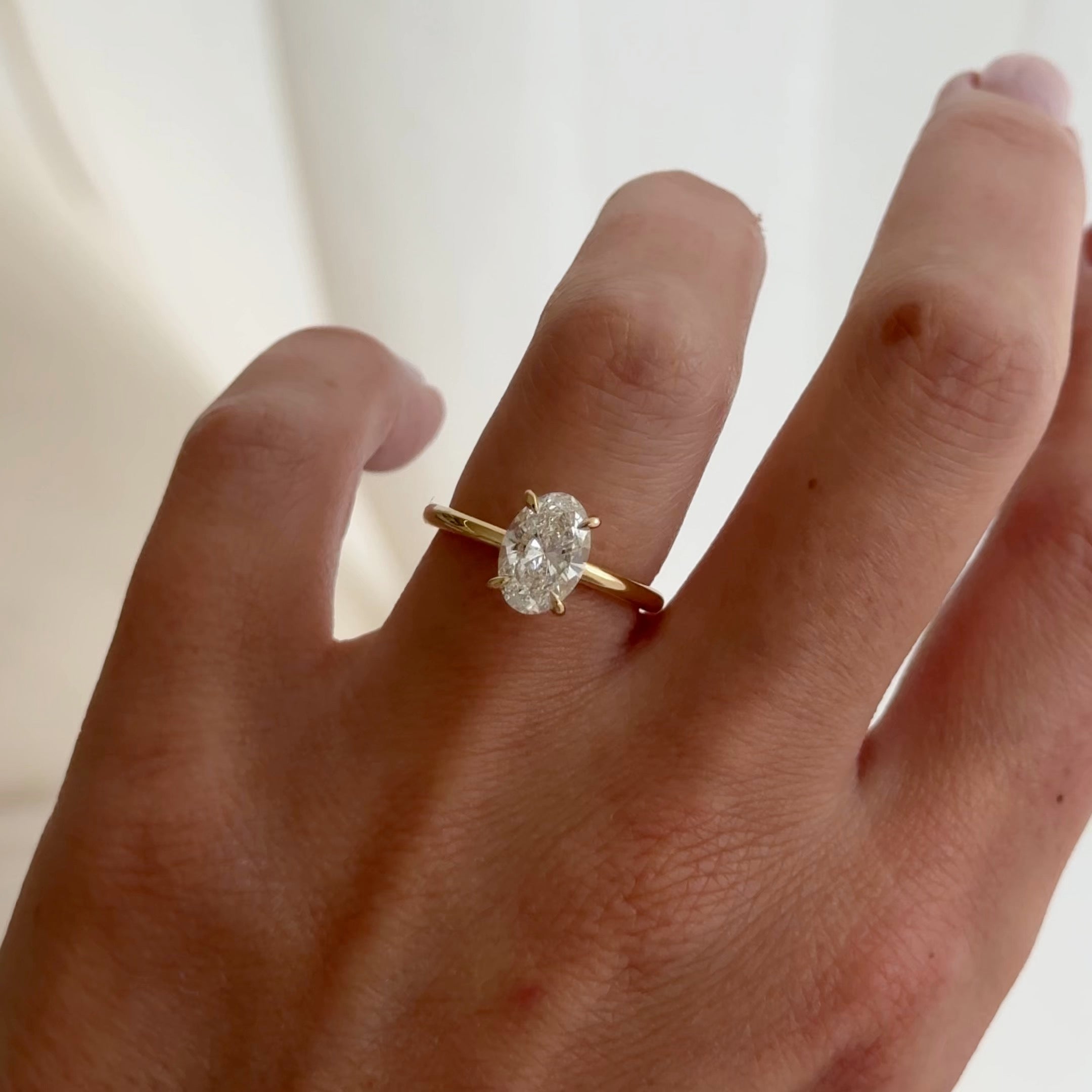 Hand wearing a luxurious gold ring with a large oval-cut diamond. The background is softly blurred, highlighting the elegance of the ring.