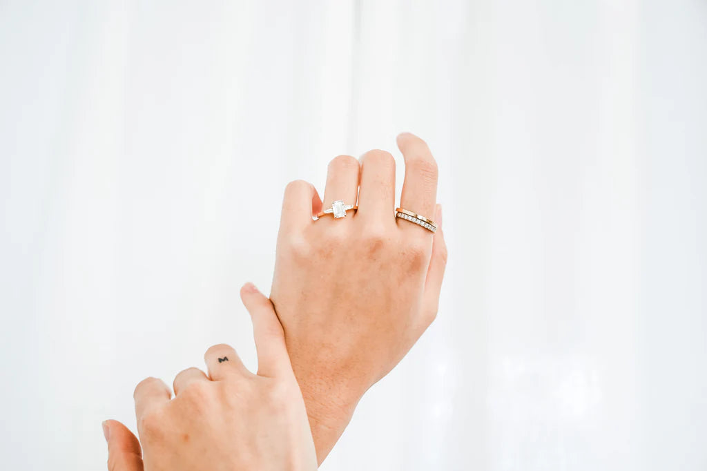 Two hands displaying luxury rings; one features a diamond solitaire, the other two gold bands with diamonds. Elegant jewellery on a white background.