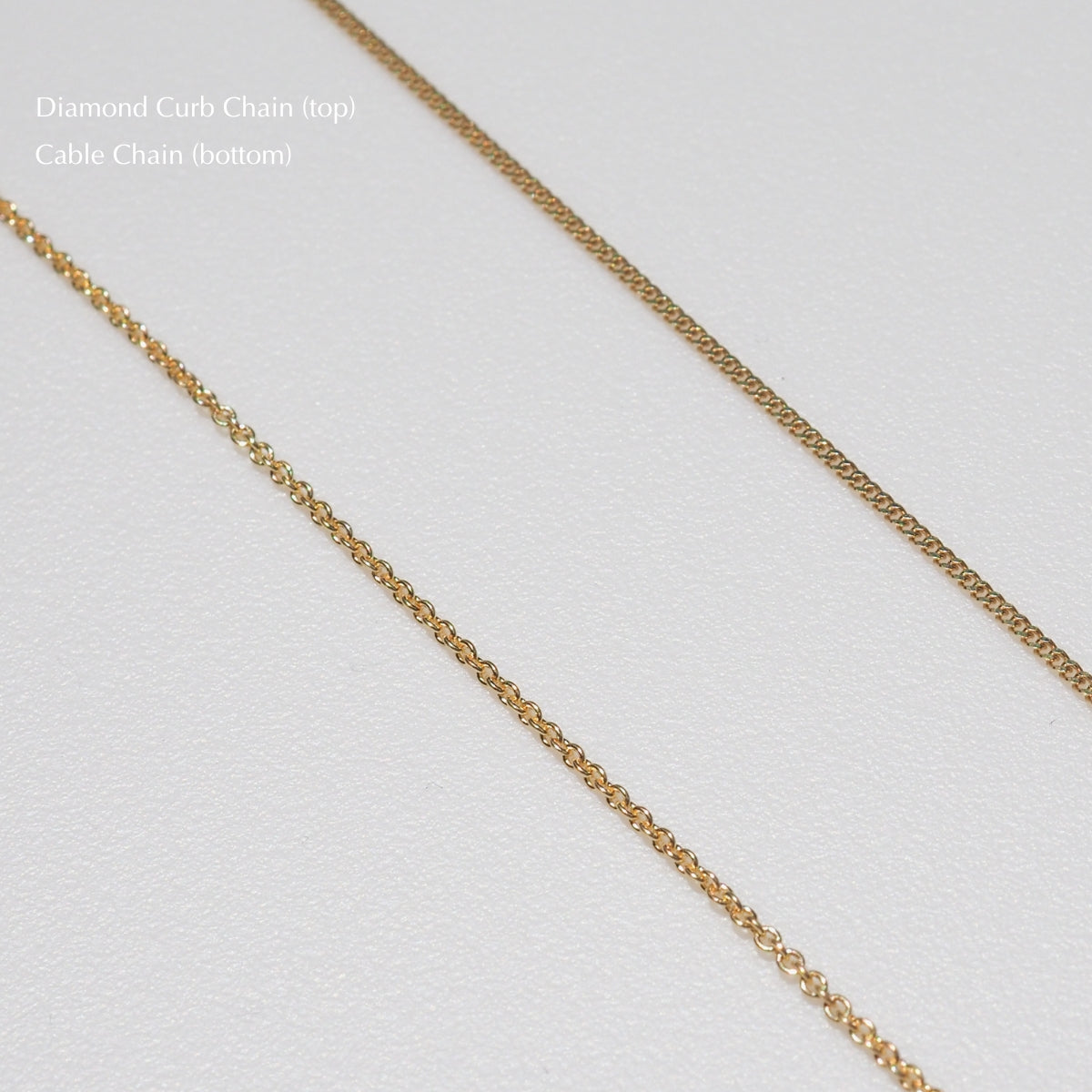 Close-up of two gold chains on a white background: a Diamond Curb Chain on top and a Cable Chain below, showcasing intricate jewellery design.