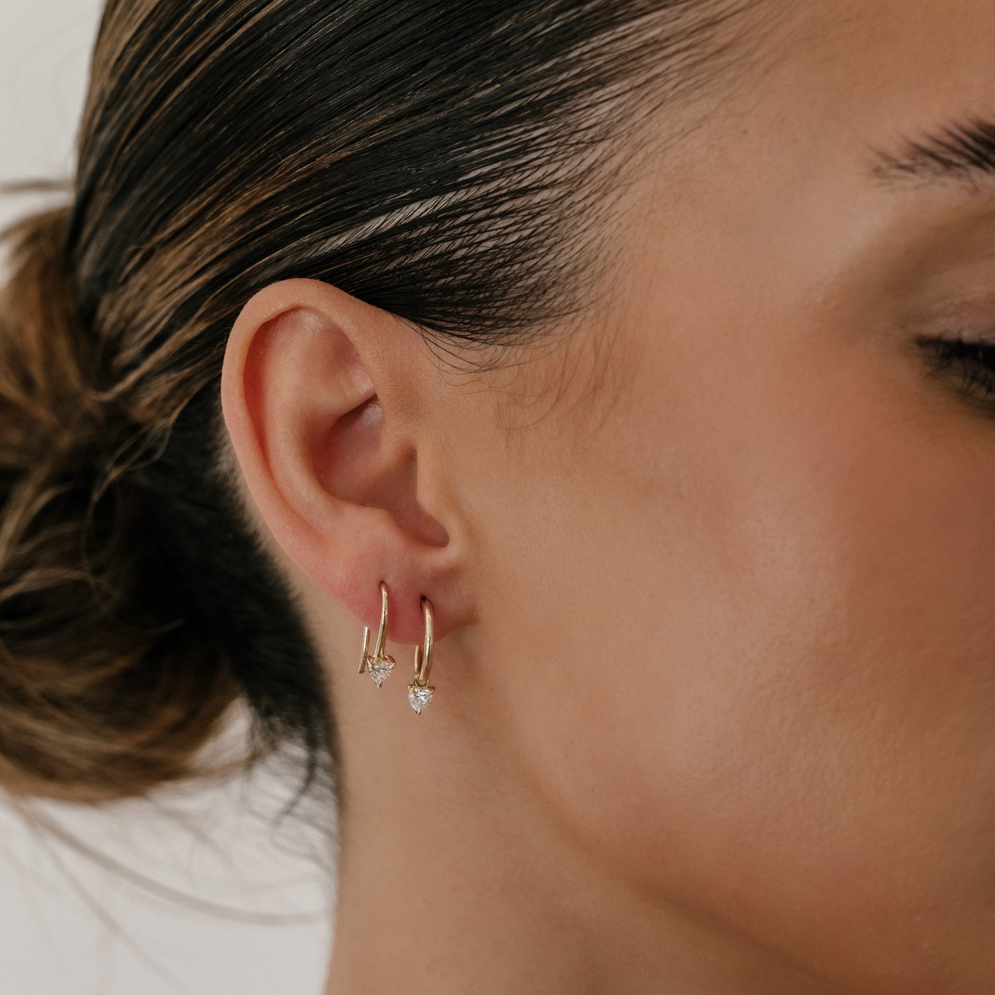 Close-up of a woman's ear wearing two elegant gold hoop earrings, one with a dangling teardrop gemstone, showcasing luxury jewellery.